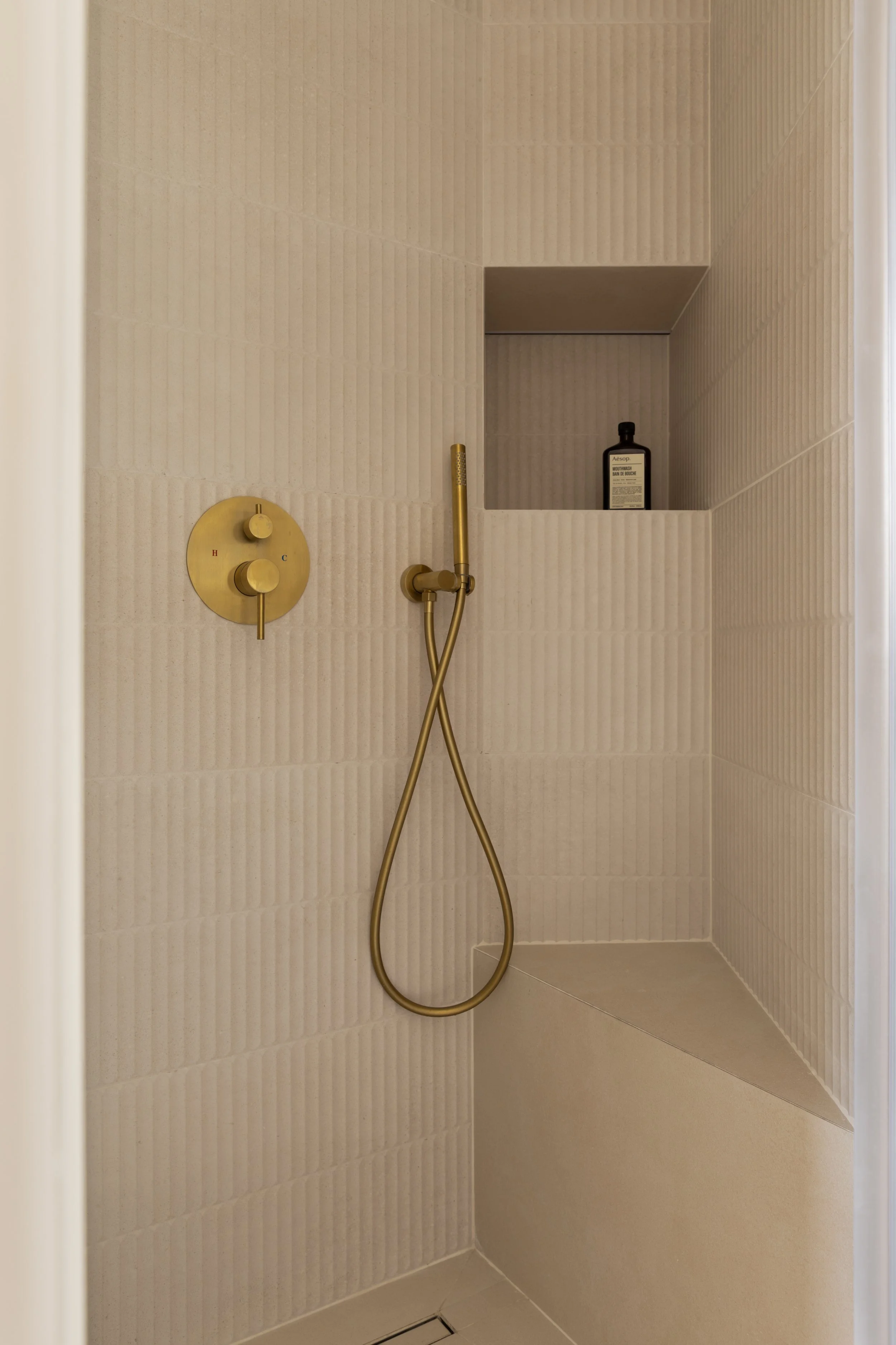 Douche à l’italienne avec robinetterie dorée et niches intégrées, design épuré.