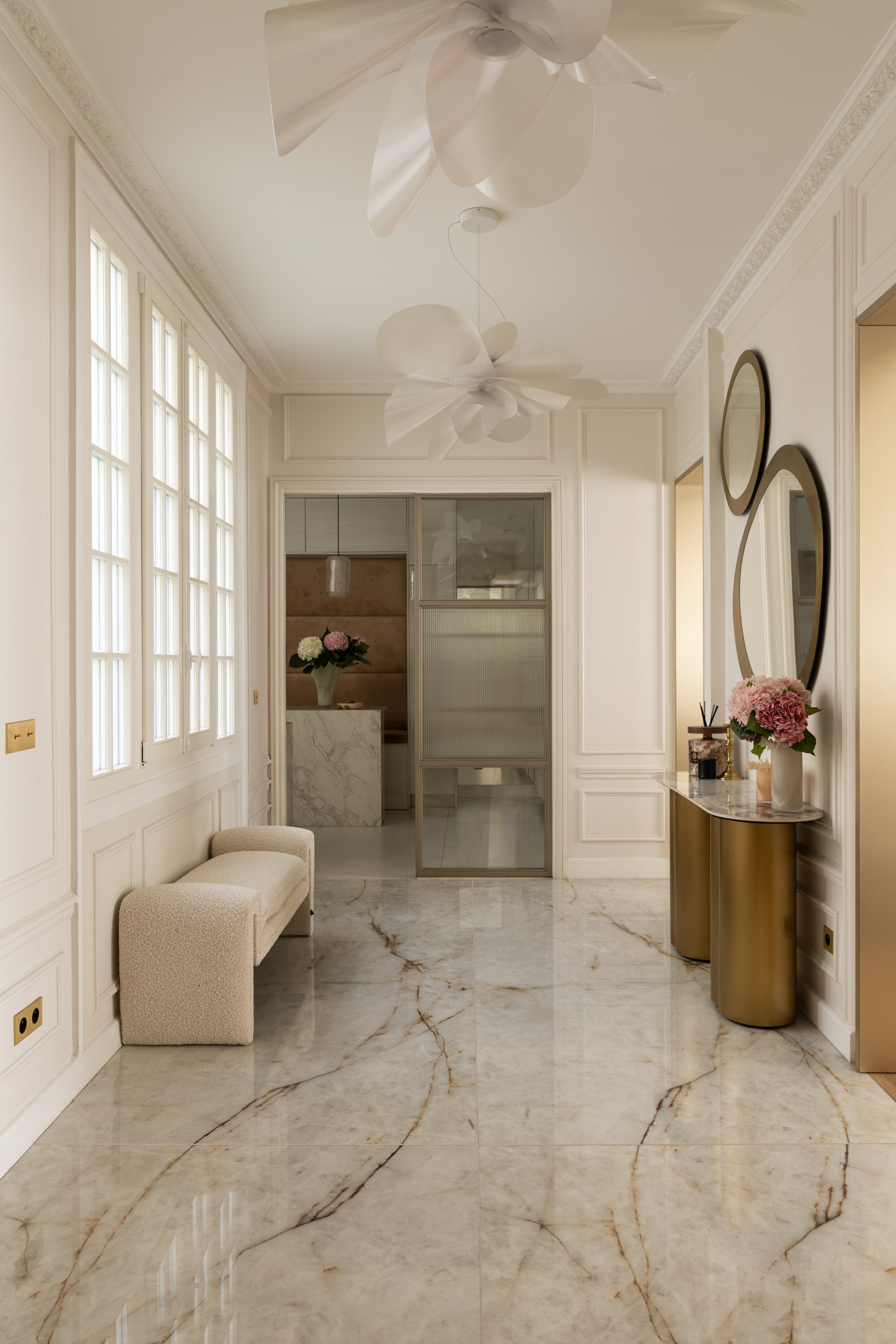 Entrée d’un appartement haussmannien à Malesherbes, Paris, avec sol en pierre veinée, moulures blanches, console dorée et suspensions sculpturales — Intérieurs Chomet.
