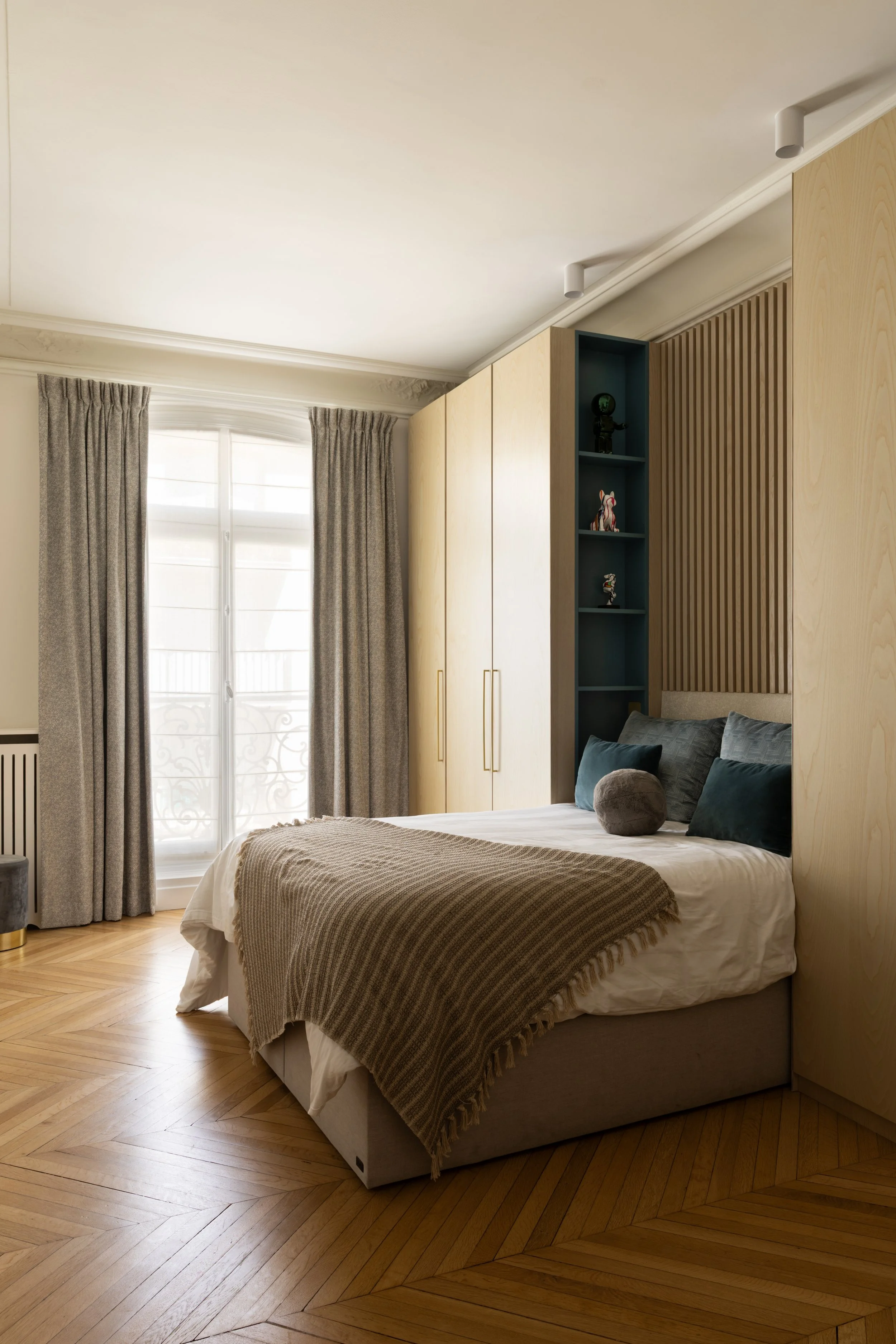 Chambre du fils dans le projet Malesherbes à Paris, avec rangements sur mesure en bois clair, tête de lit à tasseaux, niches bleu profond et parquet en point de Hongrie — Intérieurs Chomet.