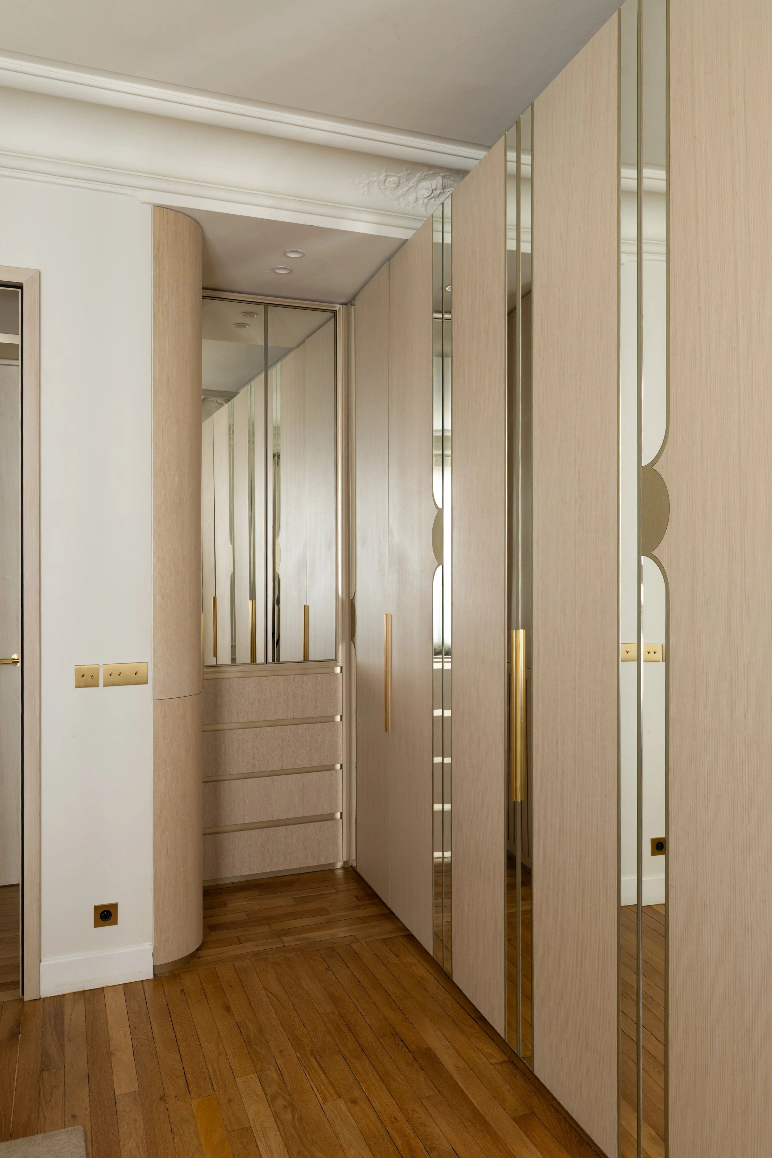 Dressing sur mesure de la chambre parentale du projet Malesherbes à Paris, avec façades en bois clair, bandes de miroir, poignées dorées et tiroirs intégrés — Intérieurs Chomet.