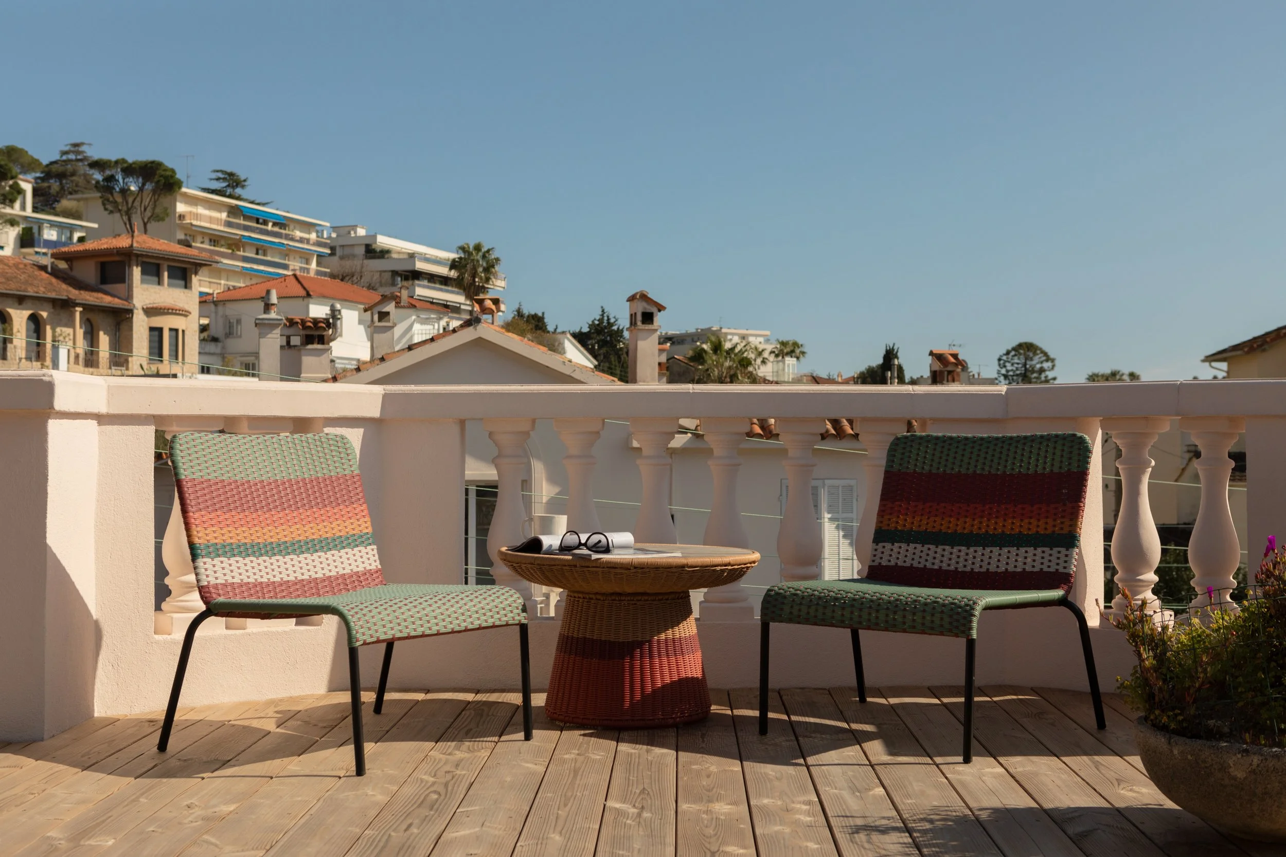 Balcon avec deux chaises modernes en plastique et un petit table en rotin, vue sur des maisons en hauteur et un ciel clair