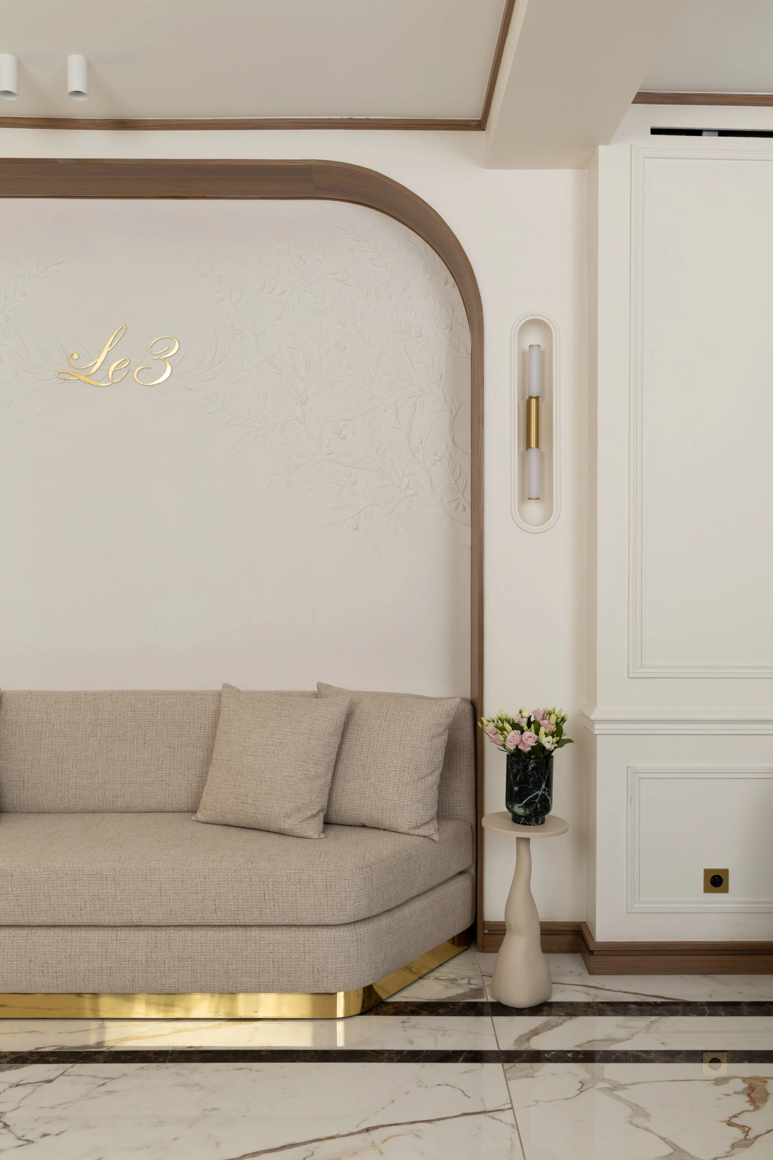 Canapé beige sur mesure, décor mural végétal en relief et finitions dorées dans un salon élégant à Paris – Intérieurs Chomet.