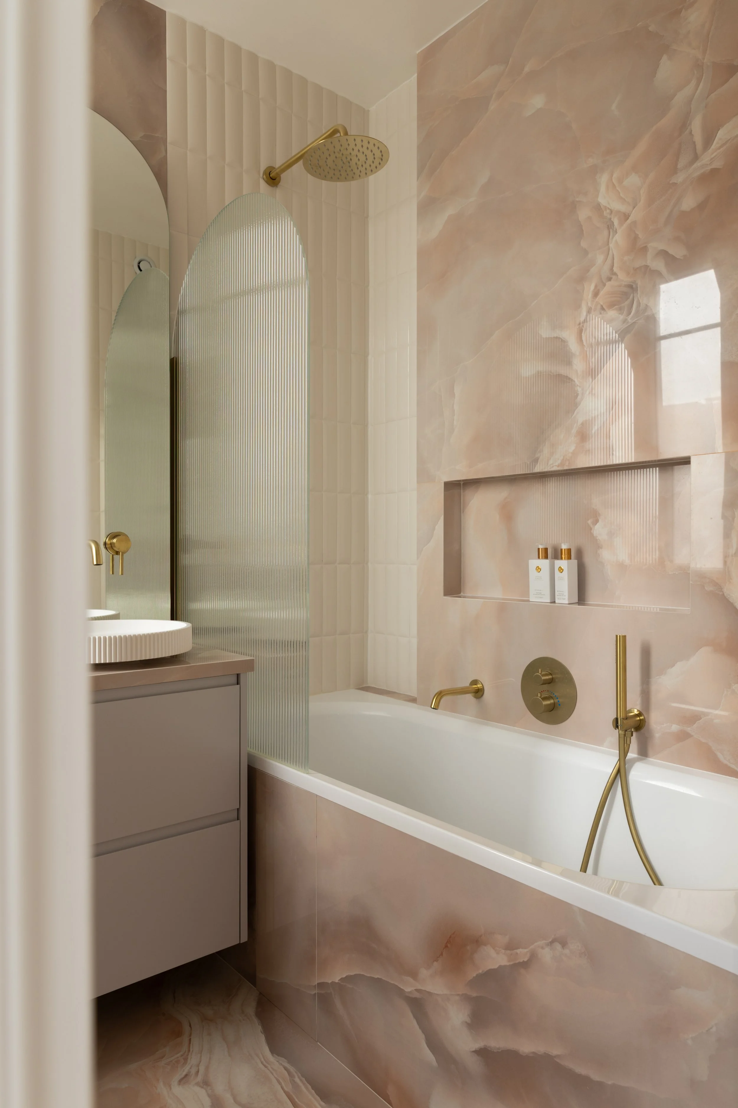 Salle de bain design aux finitions haut de gamme avec baignoire blanche, robinetterie dorée élégante et niche murale décorative. Les matériaux minéraux, les courbes architecturales et la lumière douce créent une ambiance spa chic et contemporaine.