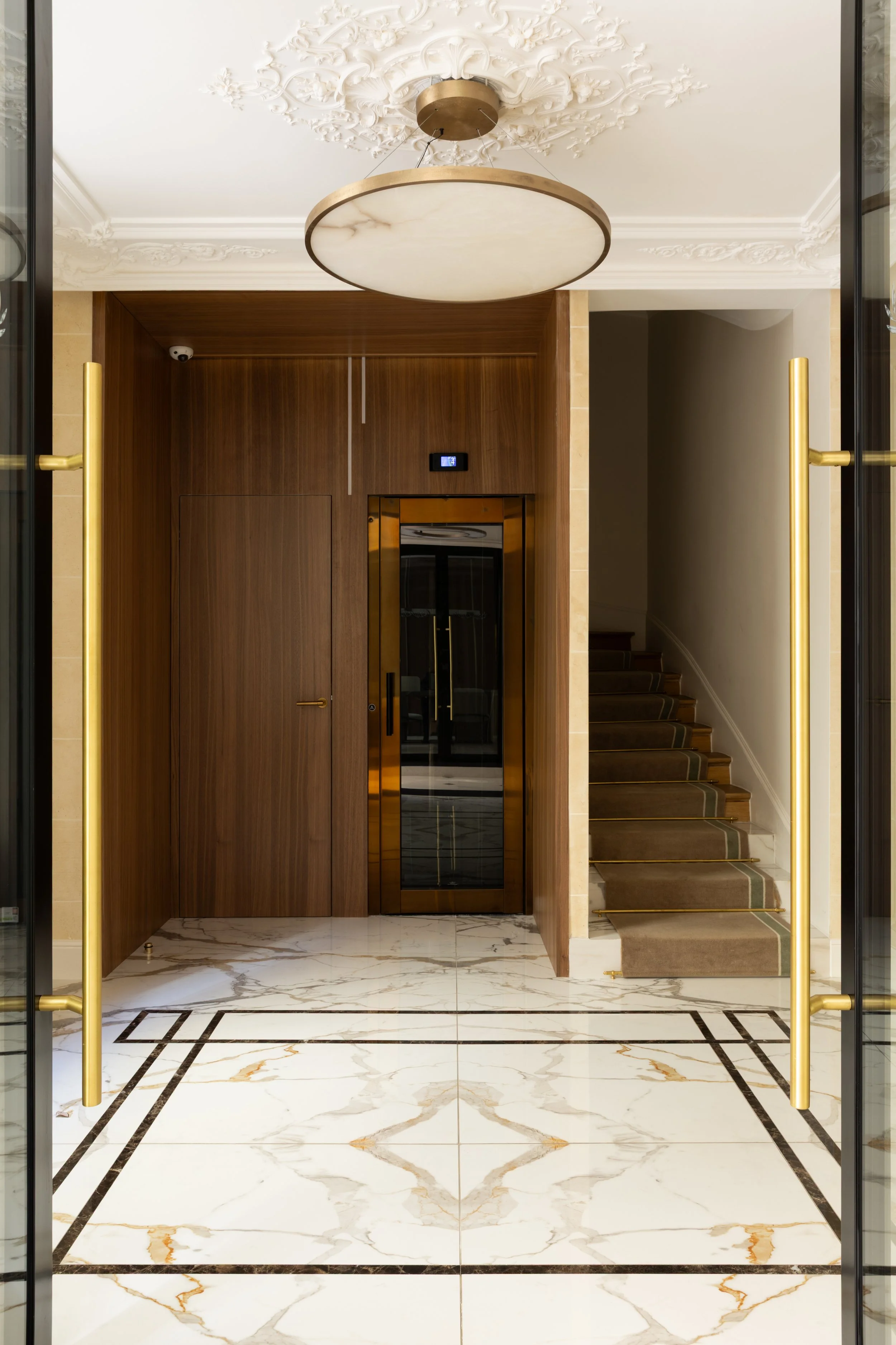 Hall d'entrée haut de gamme à Paris avec sol en marbre veiné, boiseries sur mesure, ascenseur en laiton et moulures classiques – Intérieurs Chomet.