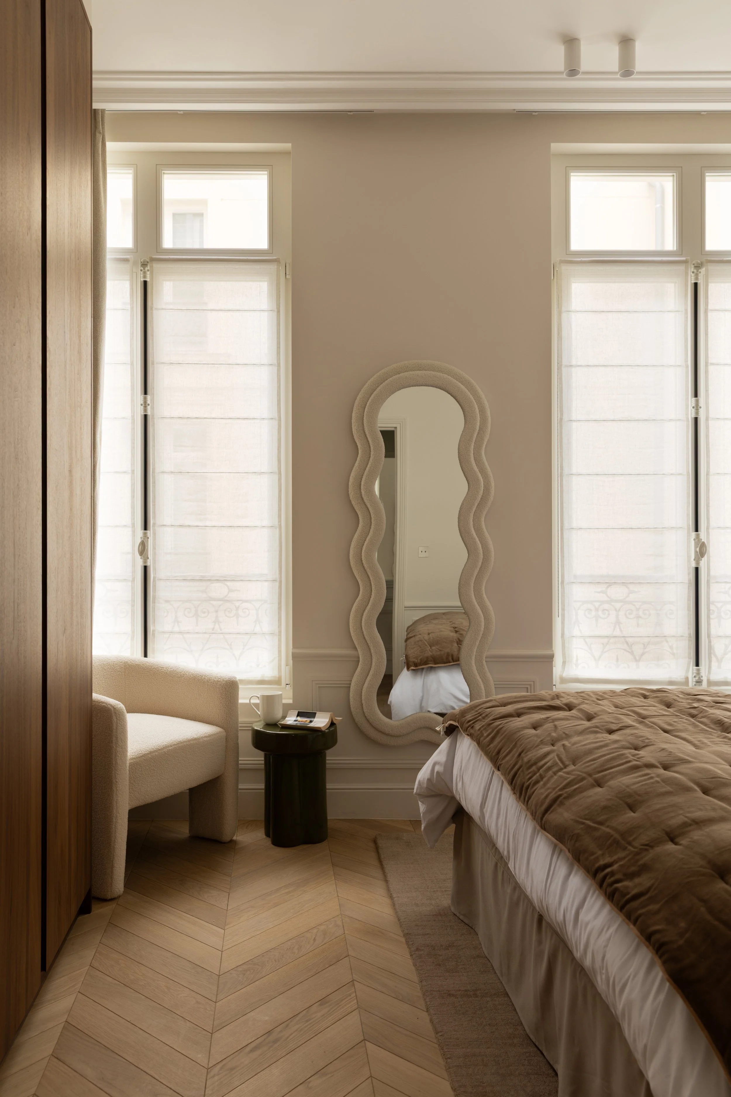 Décoration d'une chambre à Paris avec miroir aux formes organiques, fauteuil design et parquet en point de Hongrie – Intérieurs Chomet.