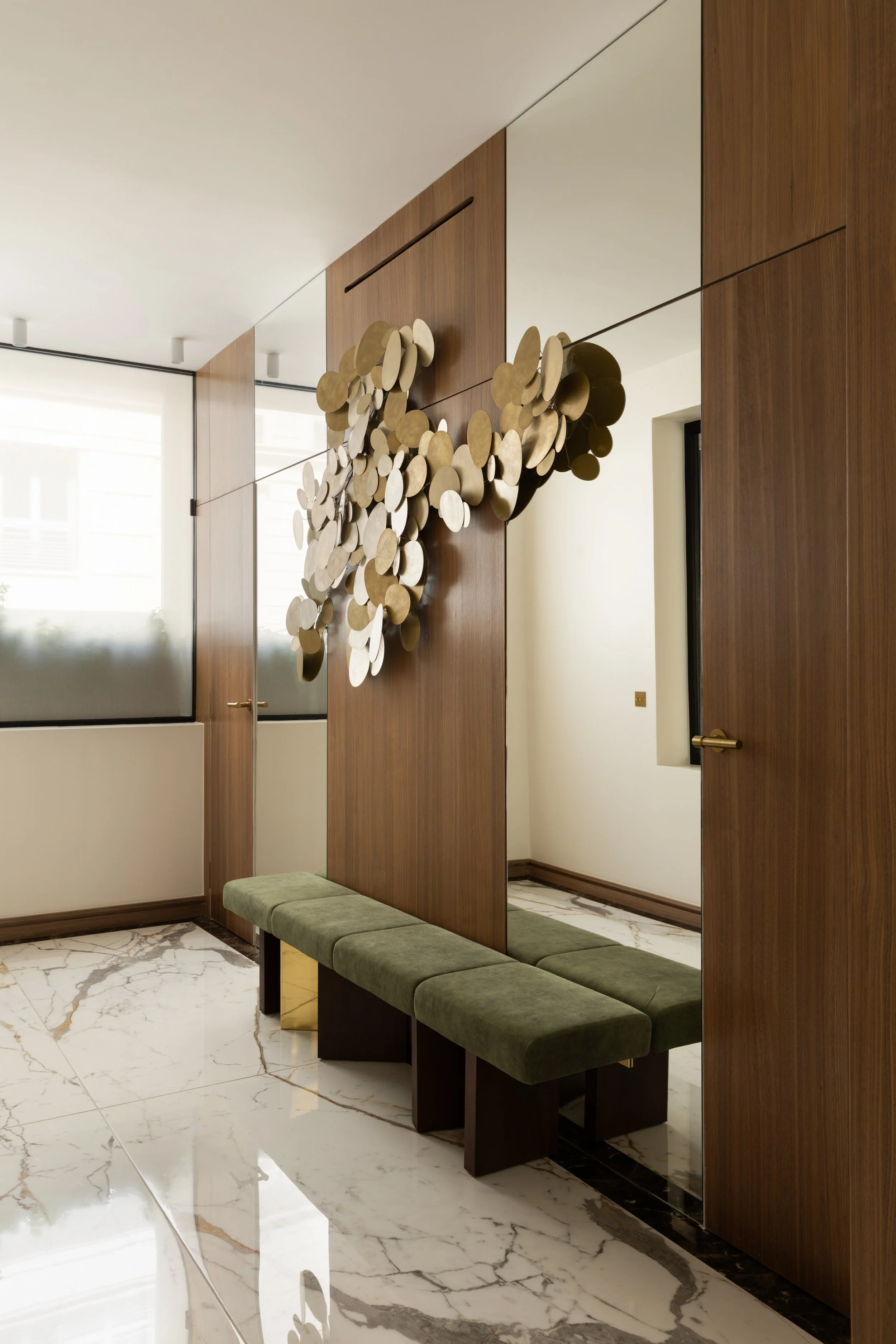 Entrée contemporaine de luxe à Paris avec sculpture murale dorée, habillage en bois, banquette en velours vert et marbre – Intérieurs Chomet.