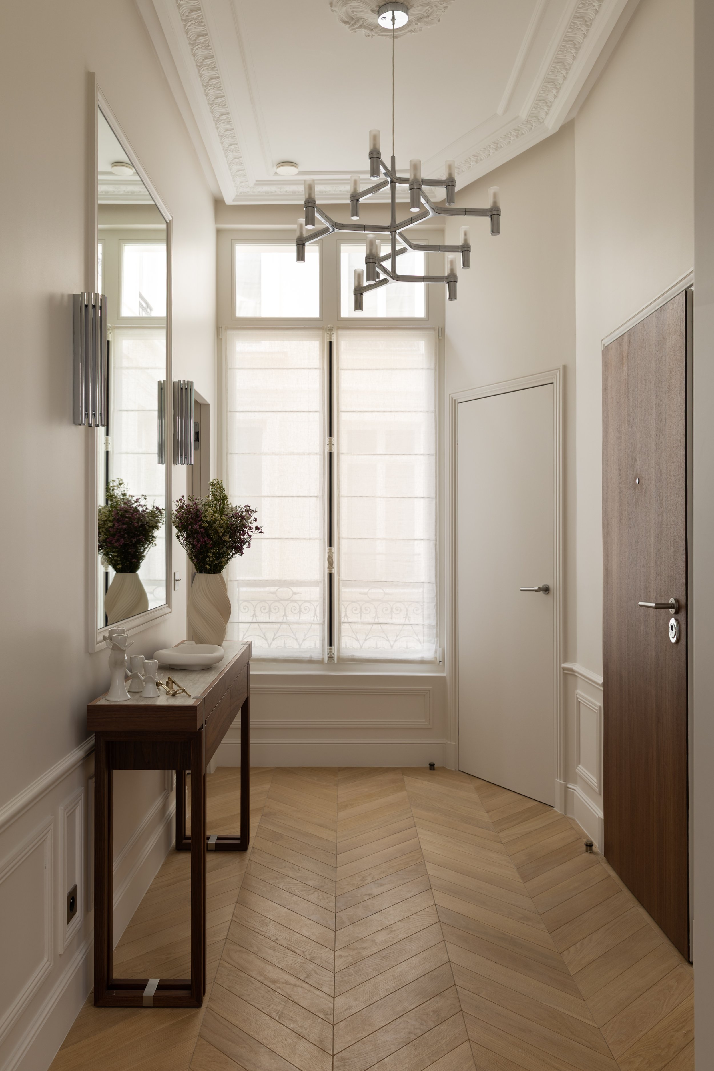 Entrée d'appartement haut de gamme à Paris avec parquet en point de Hongrie, moulures haussmanniennes et console en bois – Intérieurs Chomet.