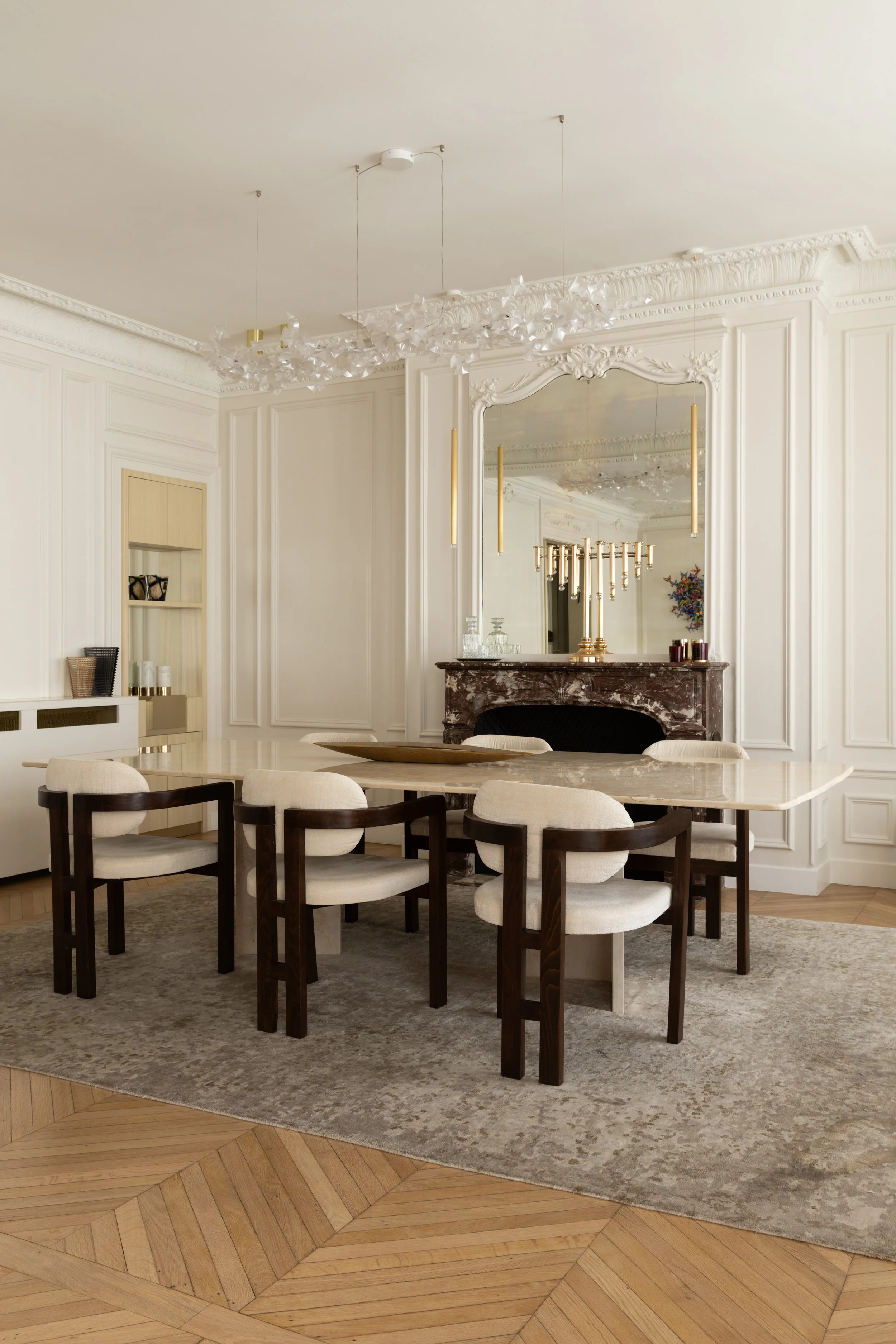 Salle à manger du projet Malesherbes à Paris, avec table en pierre veinée, chaises en bois foncé et tissu écru, cheminée en marbre et parquet en point de Hongrie — Intérieurs Chomet.