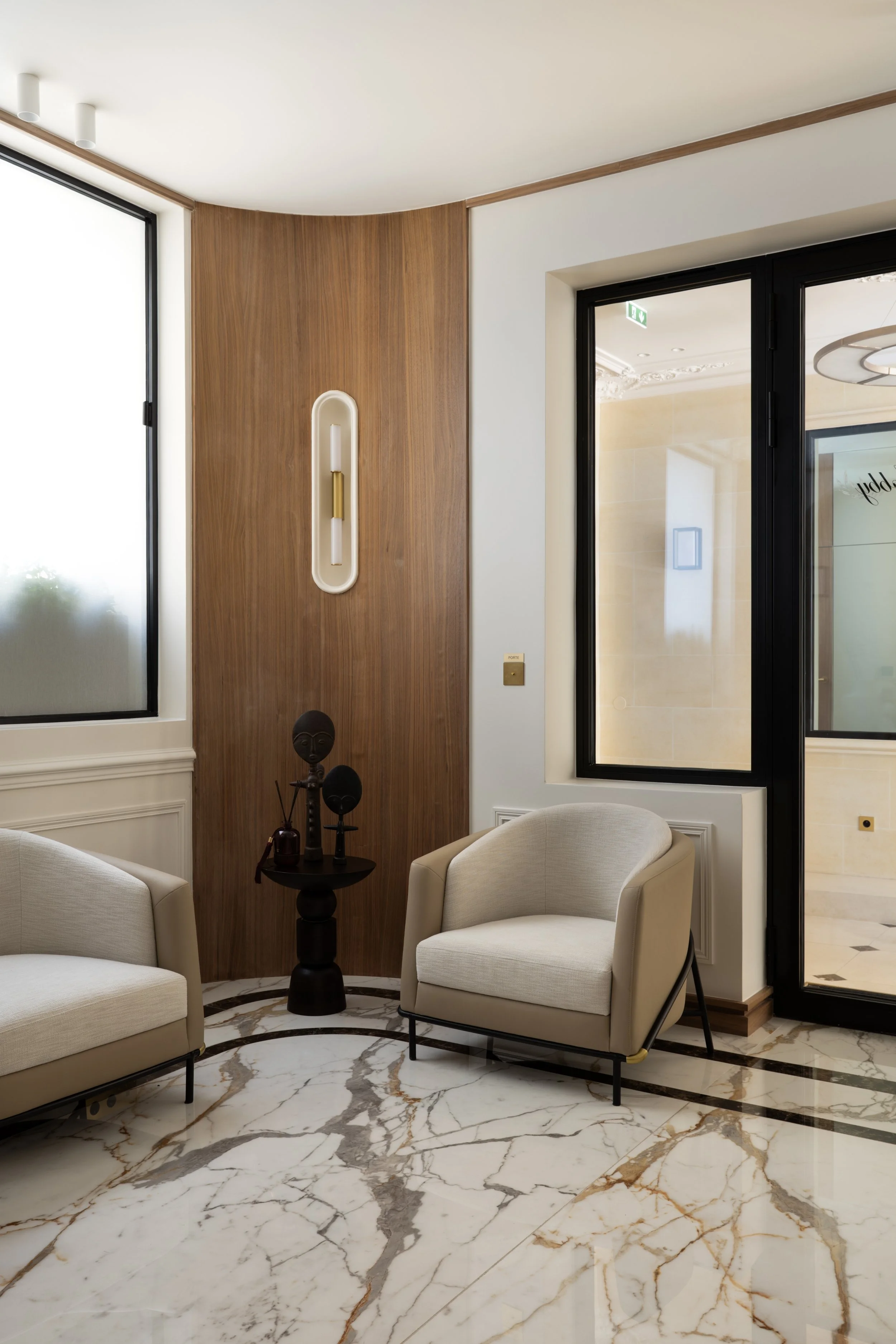 Espace d'accueil haut de gamme à Paris avec fauteuils design, boiseries sur mesure, appliques en laiton et sol en marbre veiné – Intérieurs Chomet.