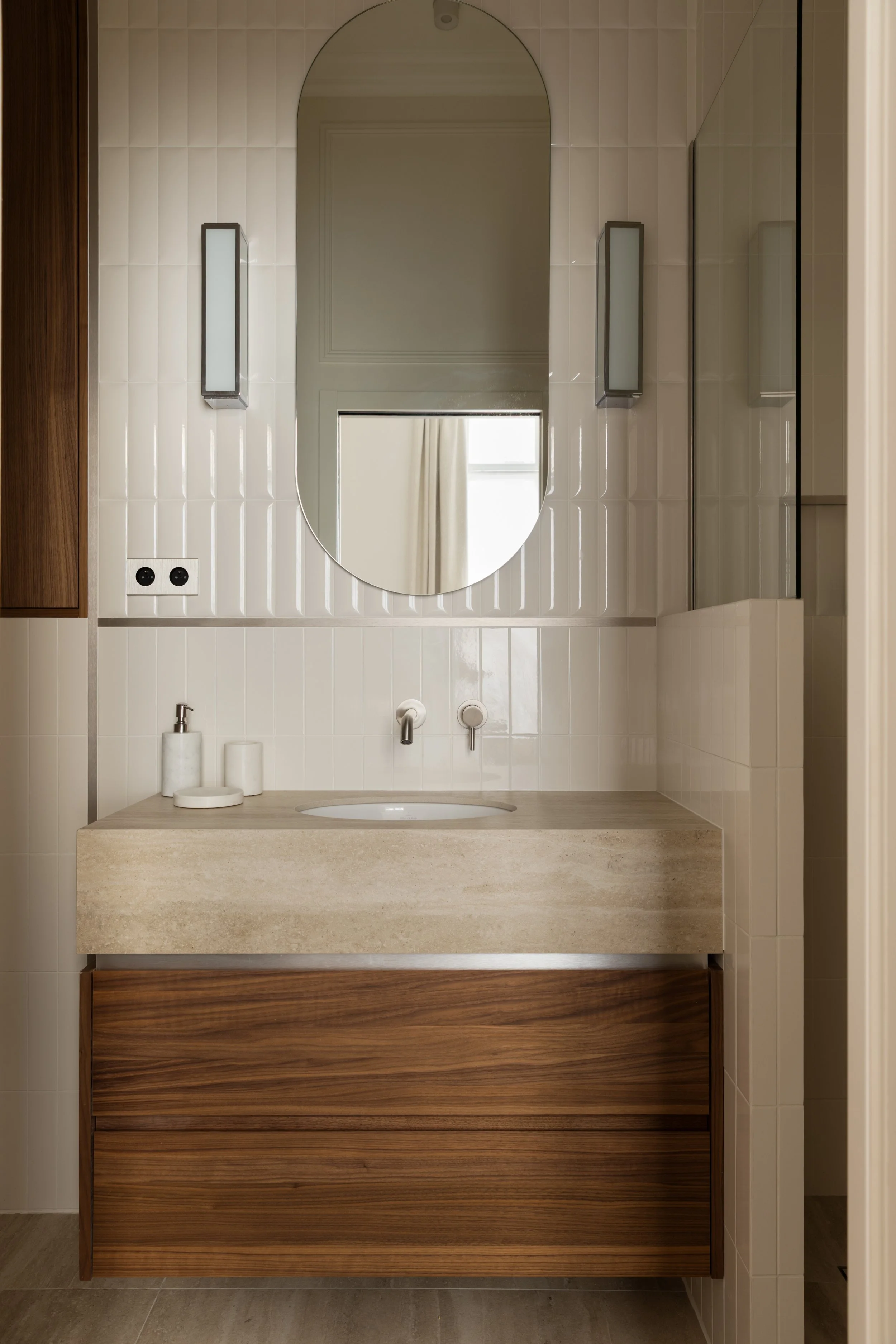 Salle de bains contemporaine à Paris avec meuble vasque en pierre naturelle, façades en bois et miroir ovale – Intérieurs Chomet.