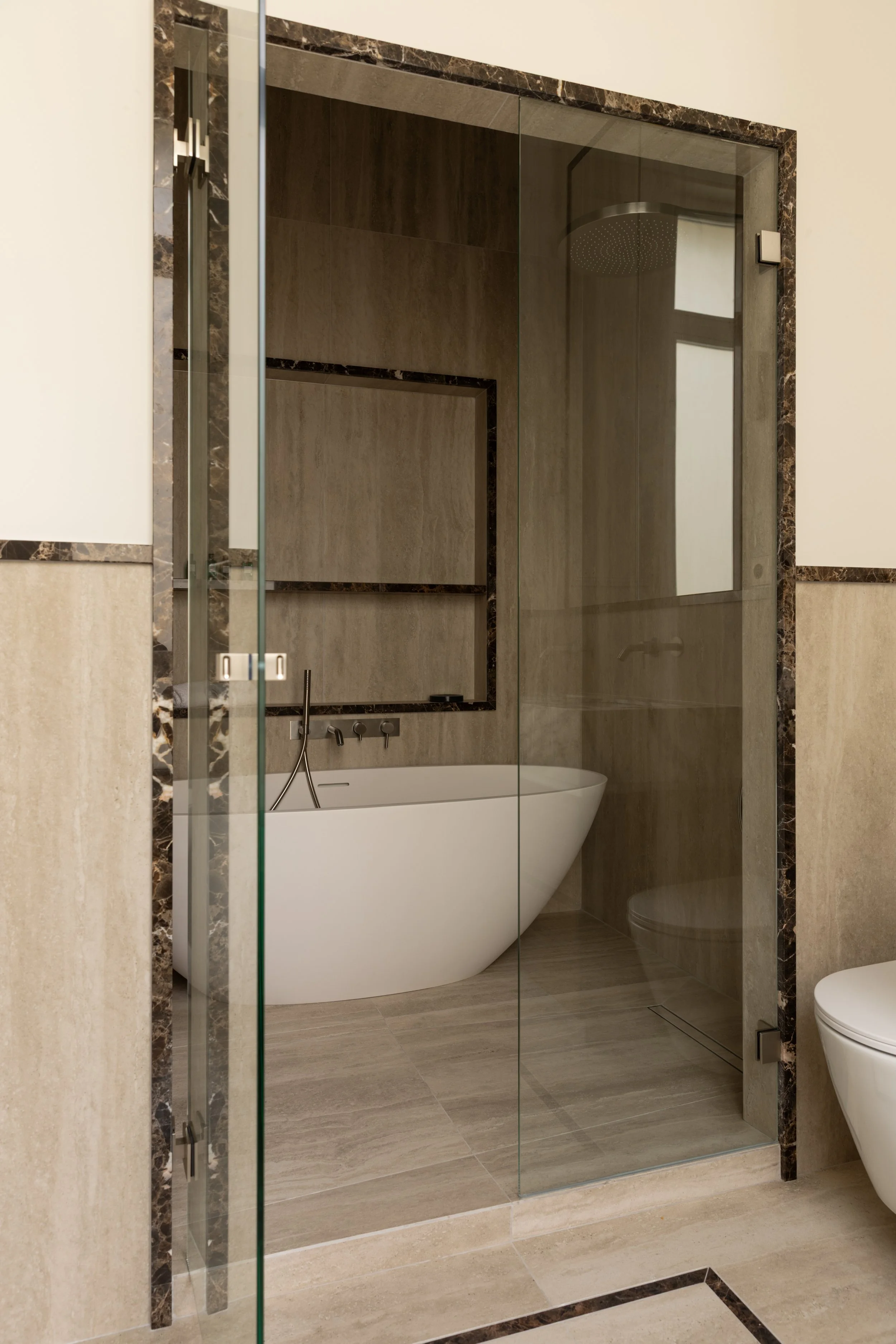Salle de bains de luxe à Paris avec baignoire îlot, douche vitrée, pierre naturelle et encadrements en marbre foncé – Intérieurs Chomet.