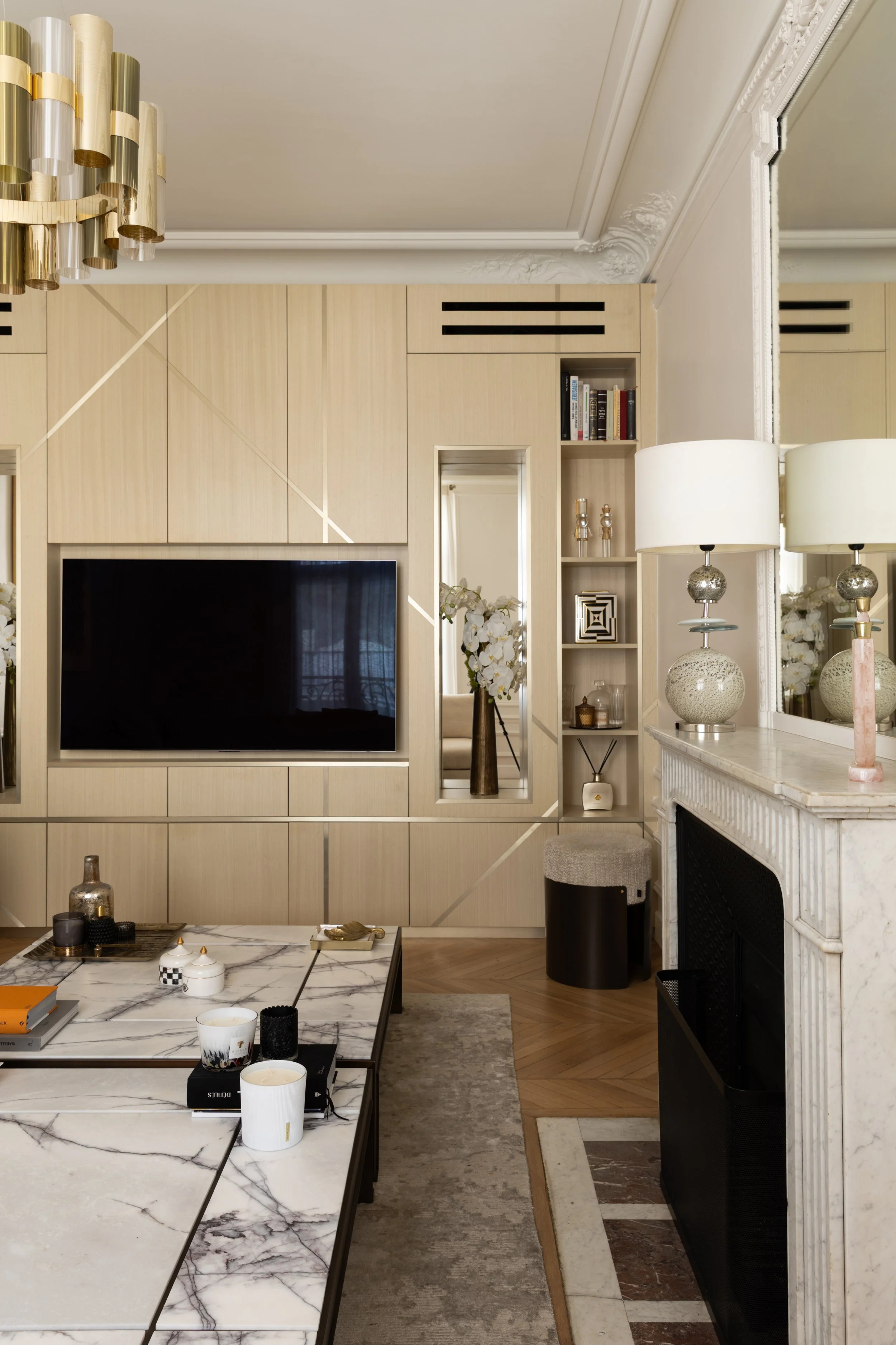 Meuble TV sur mesure en bois clair avec niches, miroirs et détails dorés, près d’une cheminée en marbre dans le projet Malesherbes à Paris — Intérieurs Chomet.