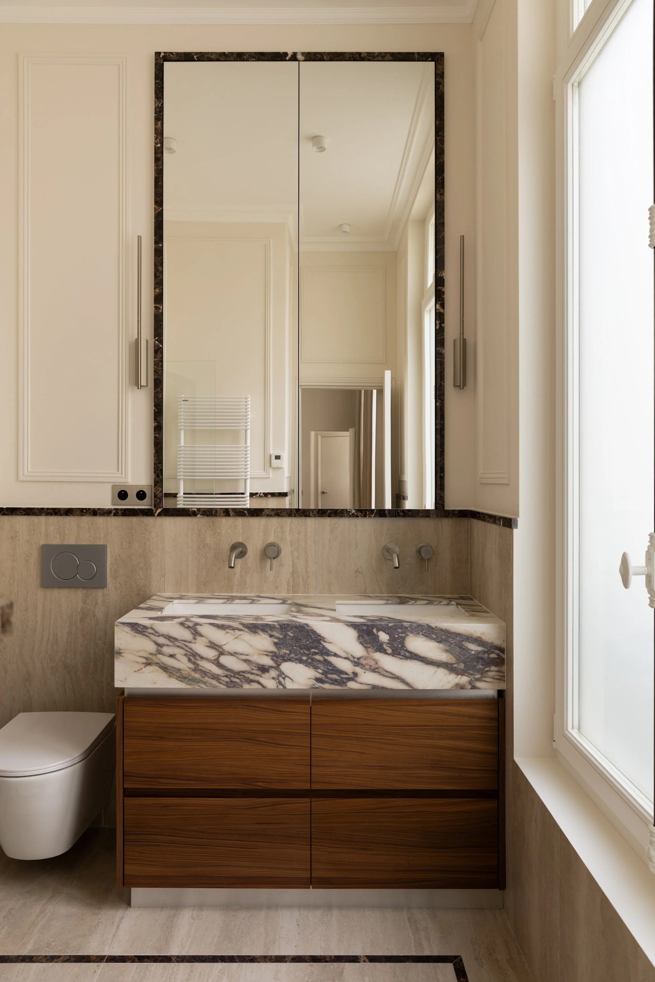 Salle de bains haut de gamme à Paris avec vasque en marbre veiné, meuble en noyer sur mesure, grand miroir et robinetterie murale – Intérieurs Chomet.