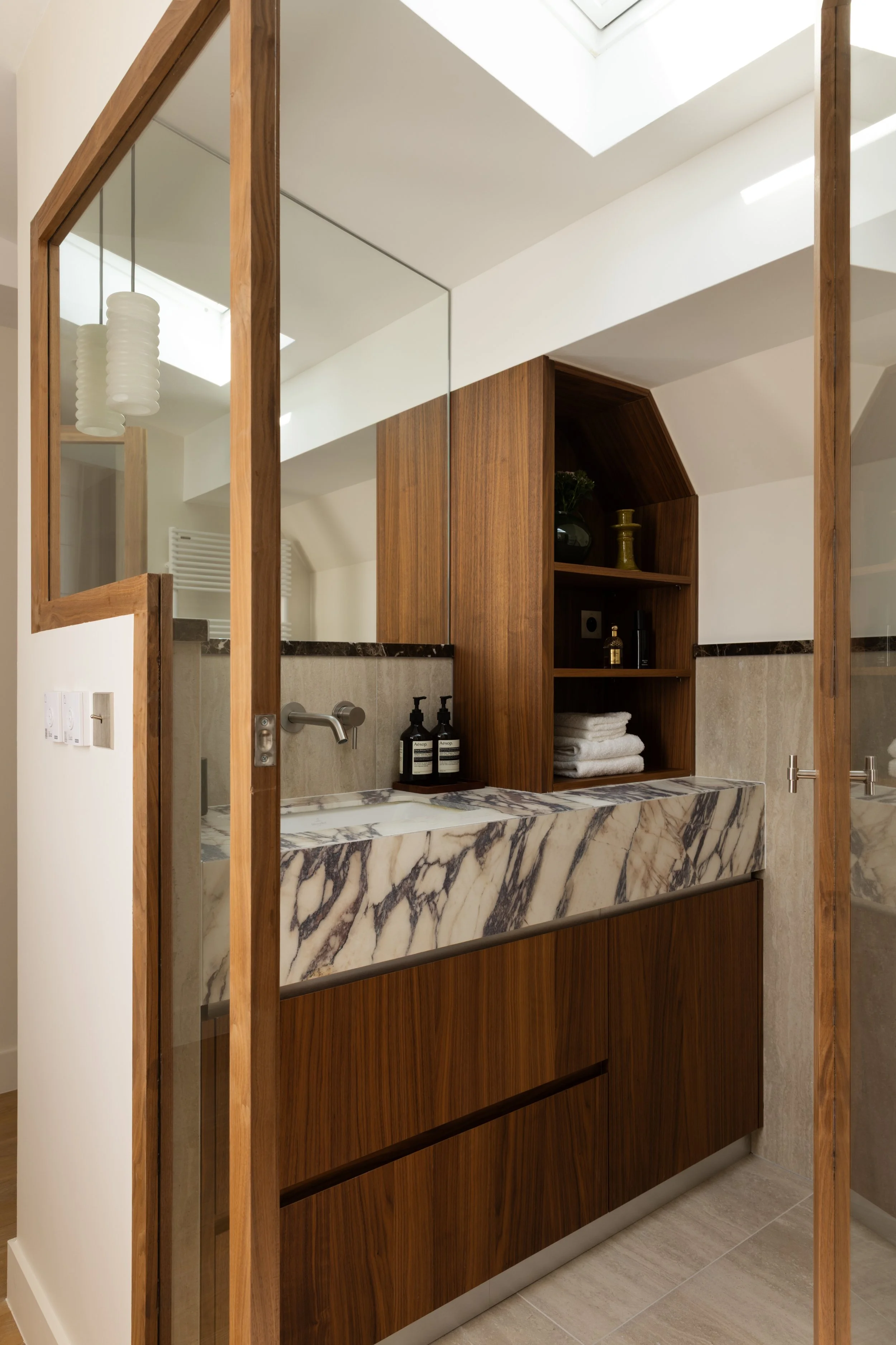 Salle de bains haut de gamme à Paris avec vasque en marbre veiné, meuble en bois sur mesure et verrière vitrée – Intérieurs Chomet.
