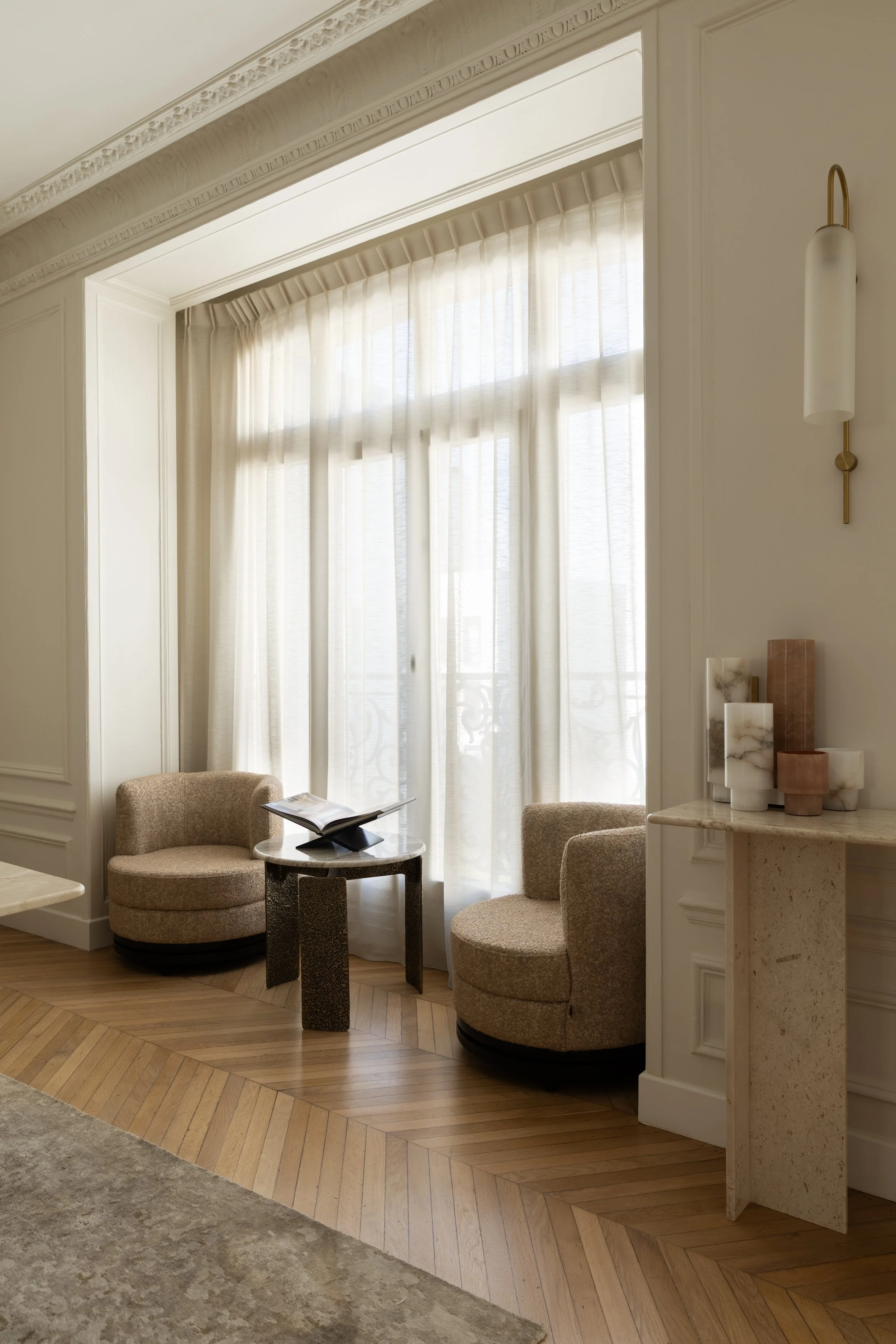 Coin lecture du projet Malesherbes à Paris, avec fauteuils arrondis en tissu beige, table d’appoint sculpturale, voilages et parquet en point de Hongrie — Intérieurs Chomet.