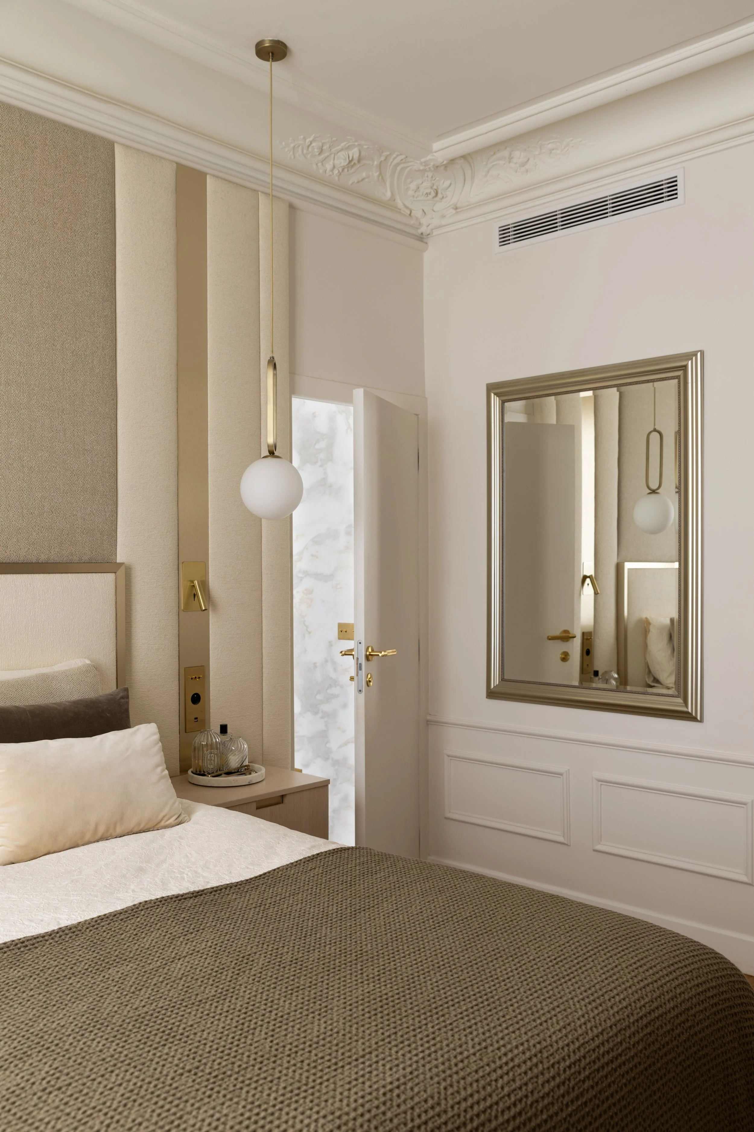 Détail de la chambre parentale du projet Malesherbes à Paris, avec miroir encadré, moulures haussmanniennes, suspension dorée à globe blanc et linge de lit écru et brun — Intérieurs Chomet.