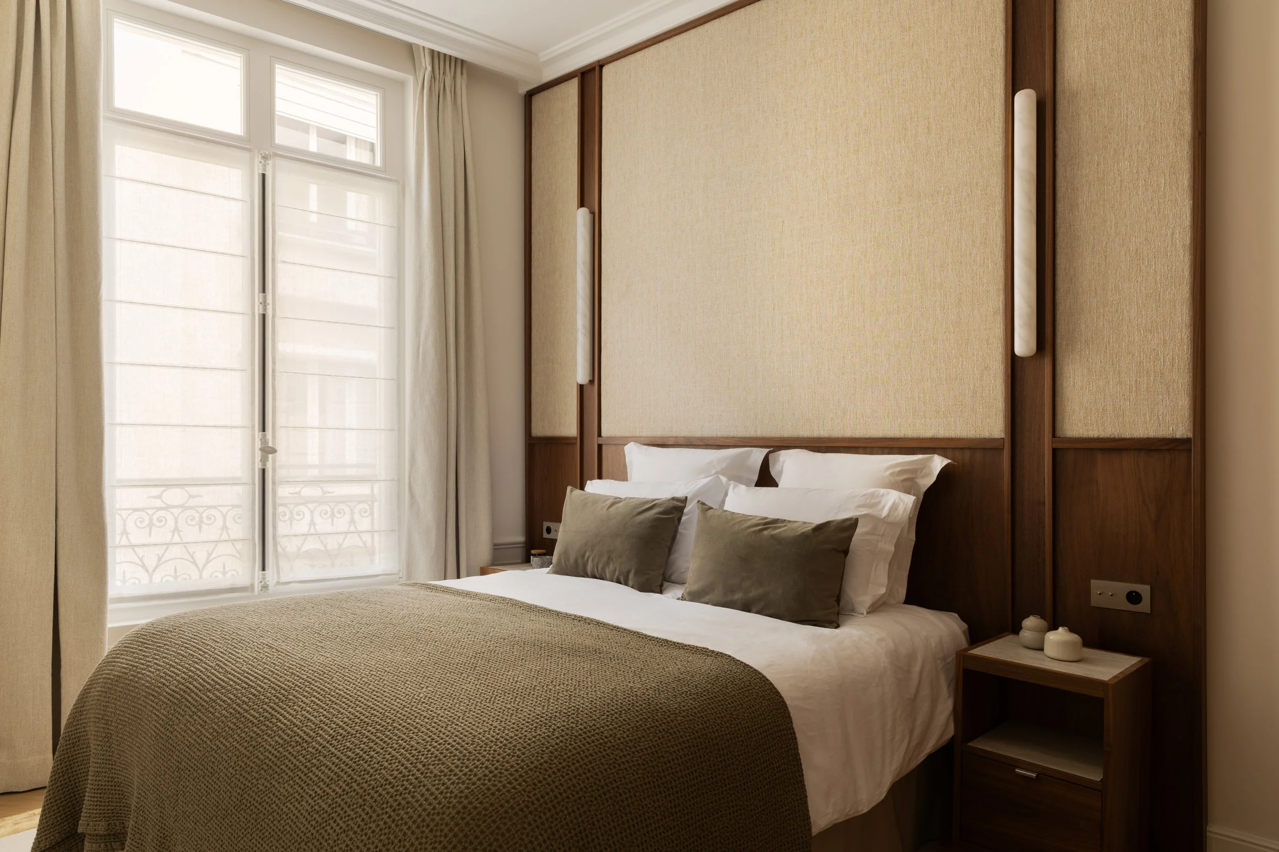 Chambre haut de gamme à Paris avec tête de lit en bois et tissu, appliques intégrées et décoration raffinée – Intérieurs Chomet.