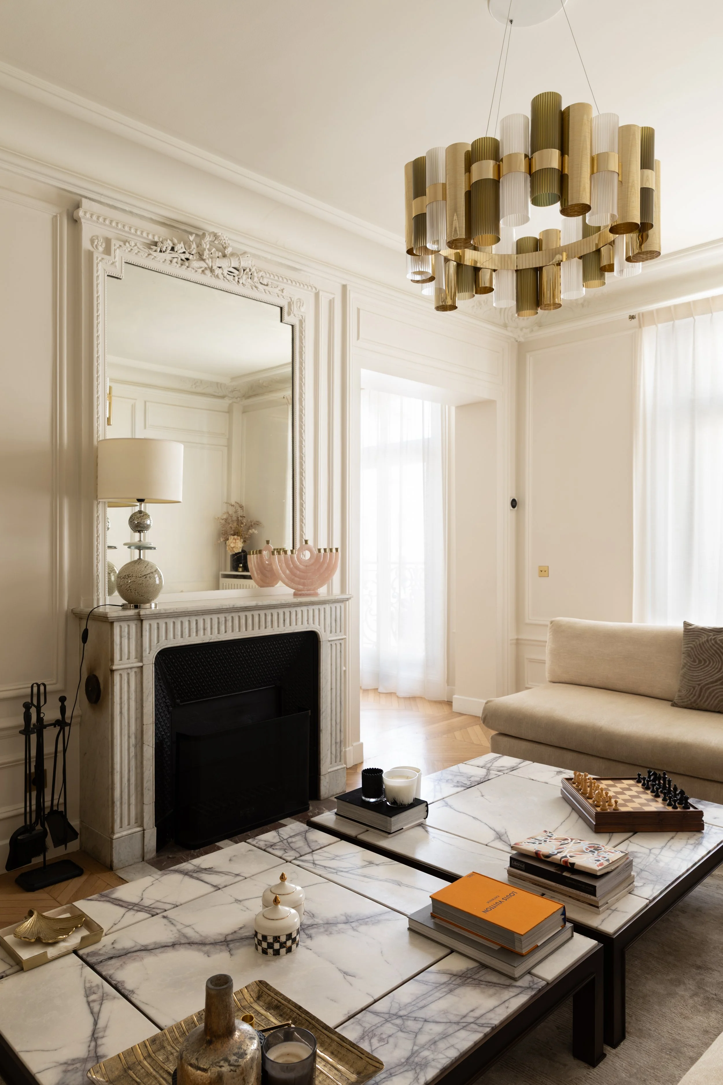 Salon TV du projet Malesherbes à Paris, avec cheminée en marbre, grand miroir mouluré, suspension dorée et tables basses en marbre veiné — Intérieurs Chomet.
