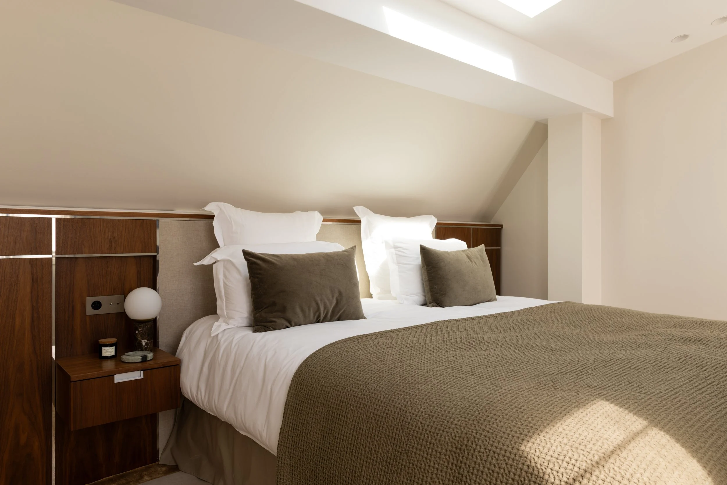 Chambre haut de gamme sous les combles à Paris, avec tête de lit en bois sur mesure, éclairage intégré et décoration raffinée – Intérieurs Chomet.