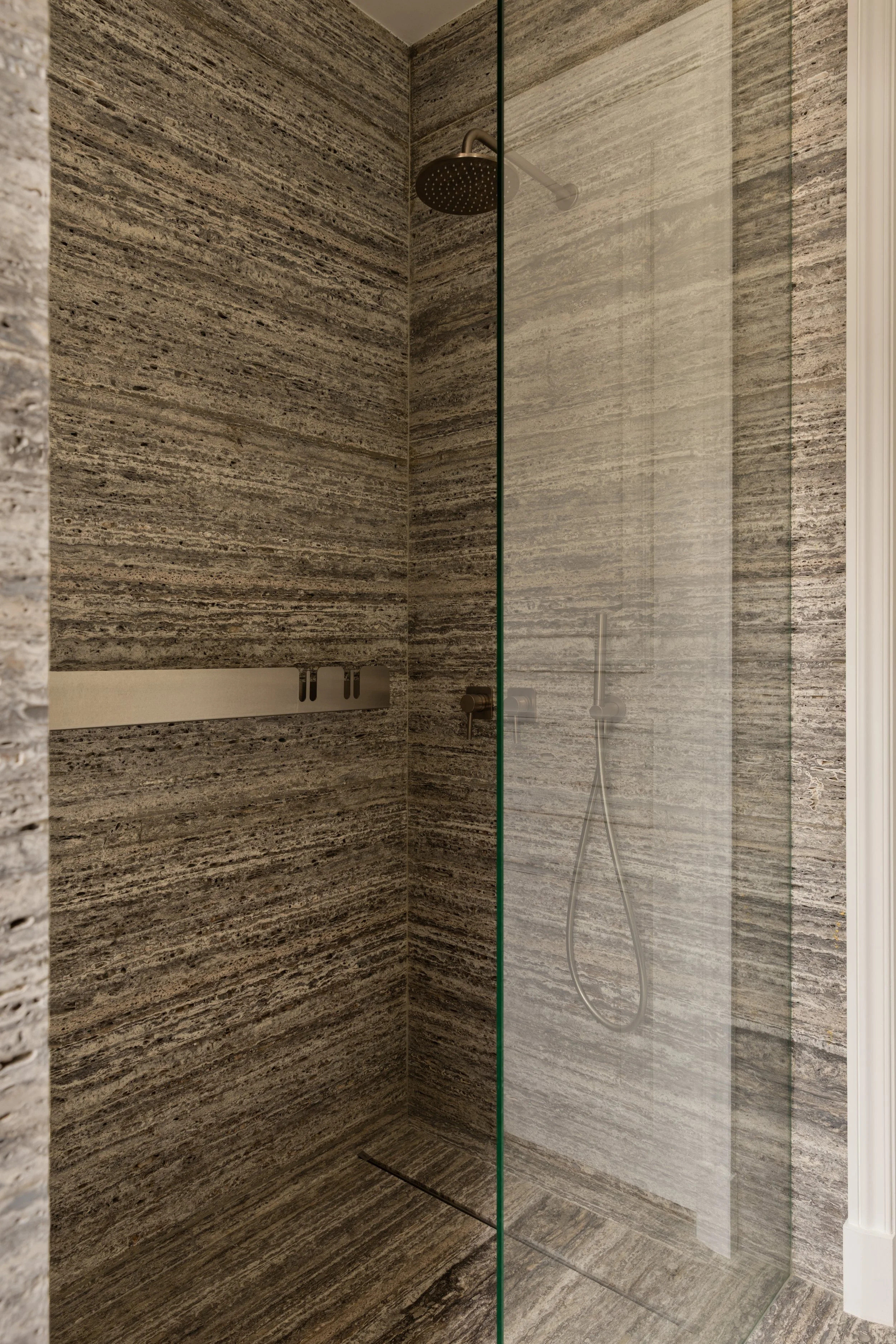 Douche en pierre naturelle avec paroi vitrée, décoration de salle de bain haut de gamme à Paris.