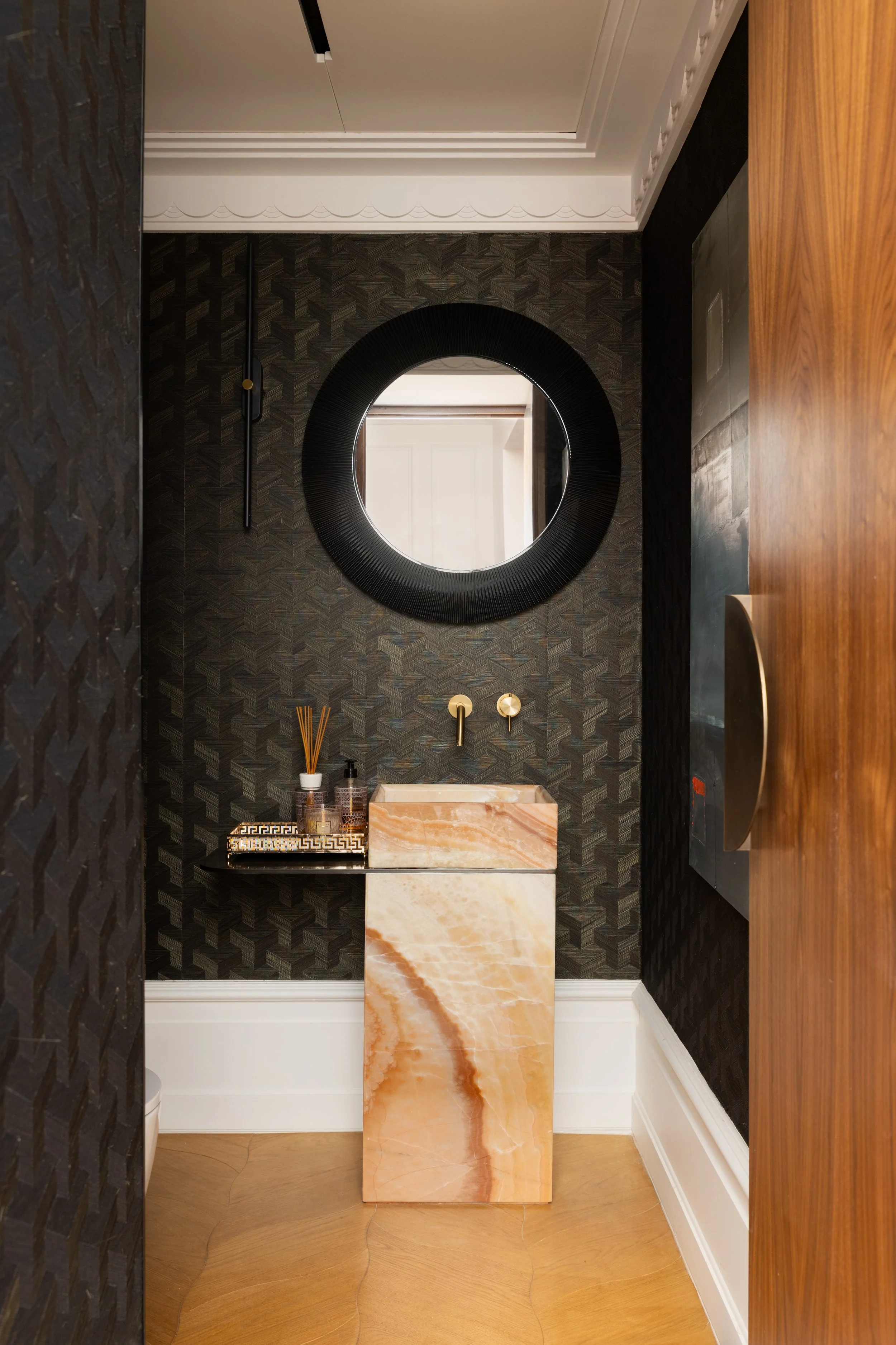 Détail de vasque sculpturale en onyx rose sur fond noir en papier peint paille de chez Arte et miroir rond, décoration intérieure haut de gamme.