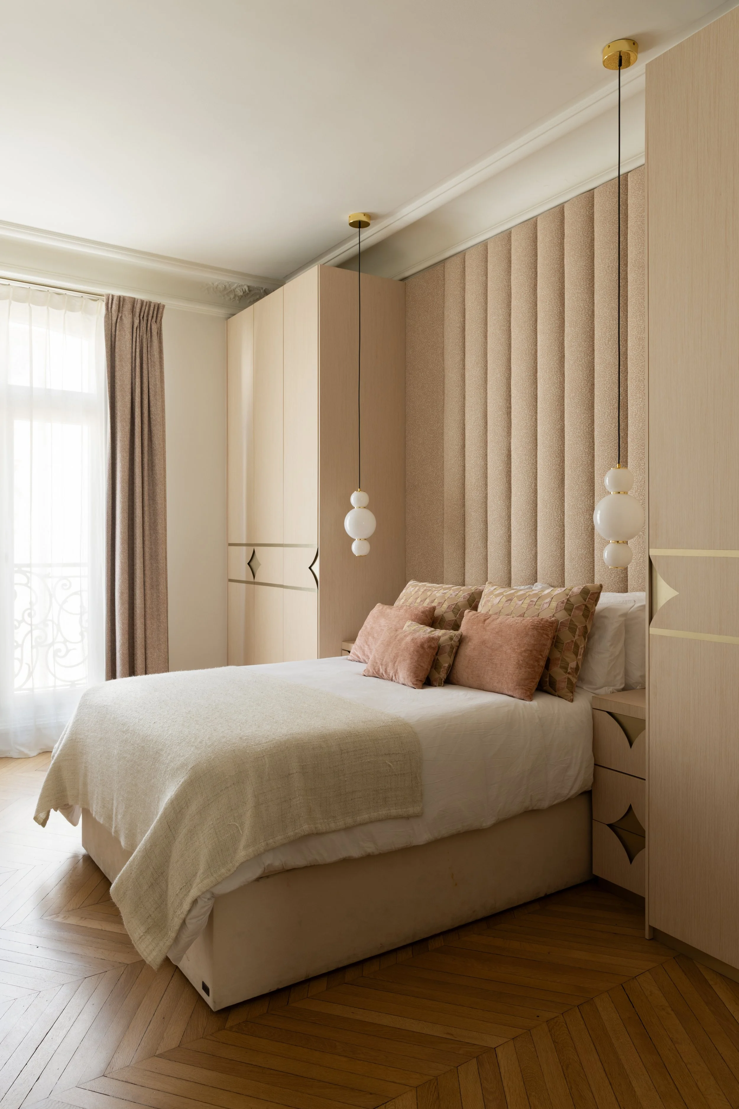 Chambre de la fille dans le projet Malesherbes à Paris, avec tête de lit tapissée, rangements sur mesure en bois clair, coussins rosés et parquet en point de Hongrie — Intérieurs Chomet.