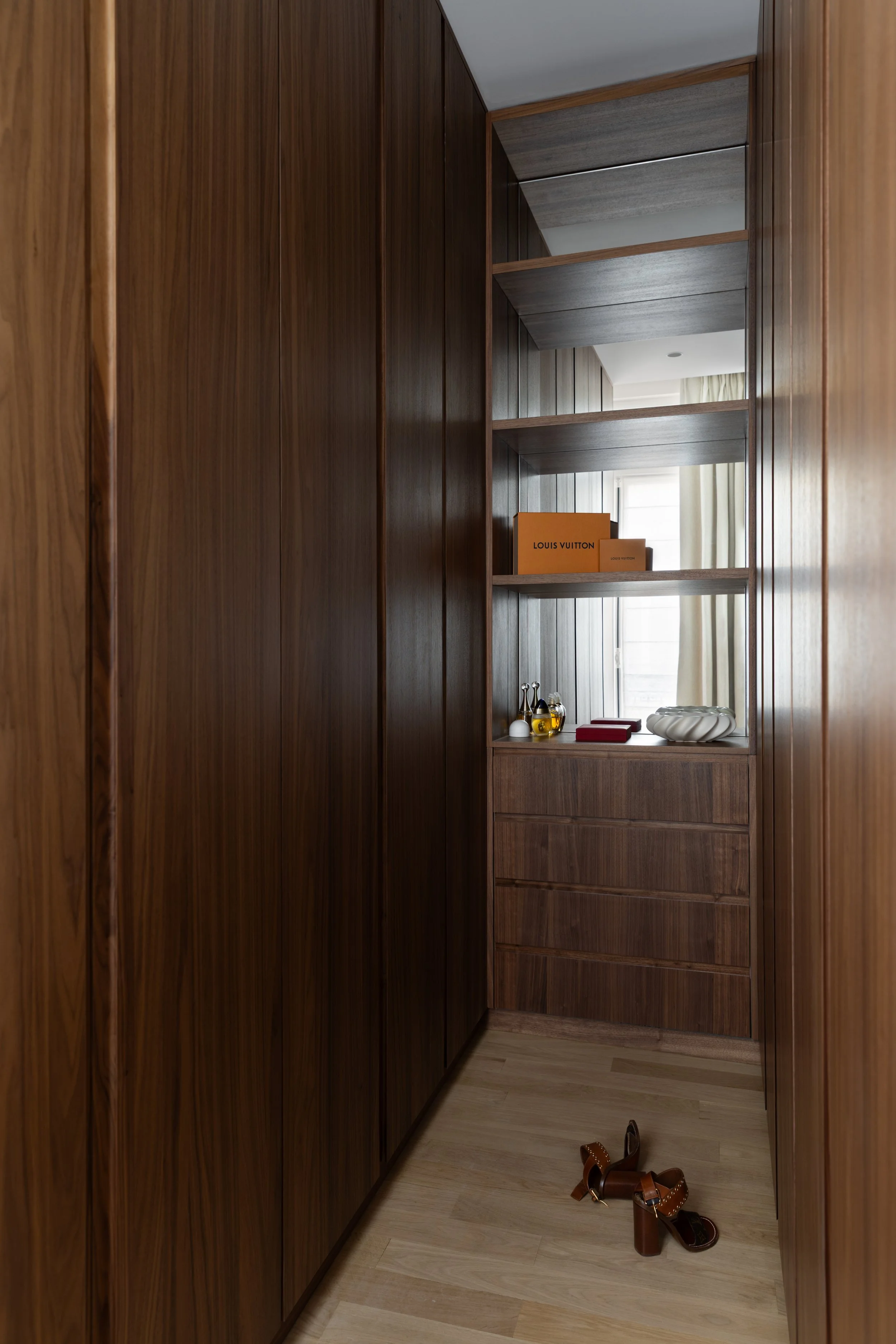 Aménagement d'un dressing haut de gamme à Paris avec placards en bois foncé, étagères ouvertes et rangements sur mesure – Intérieurs Chomet.