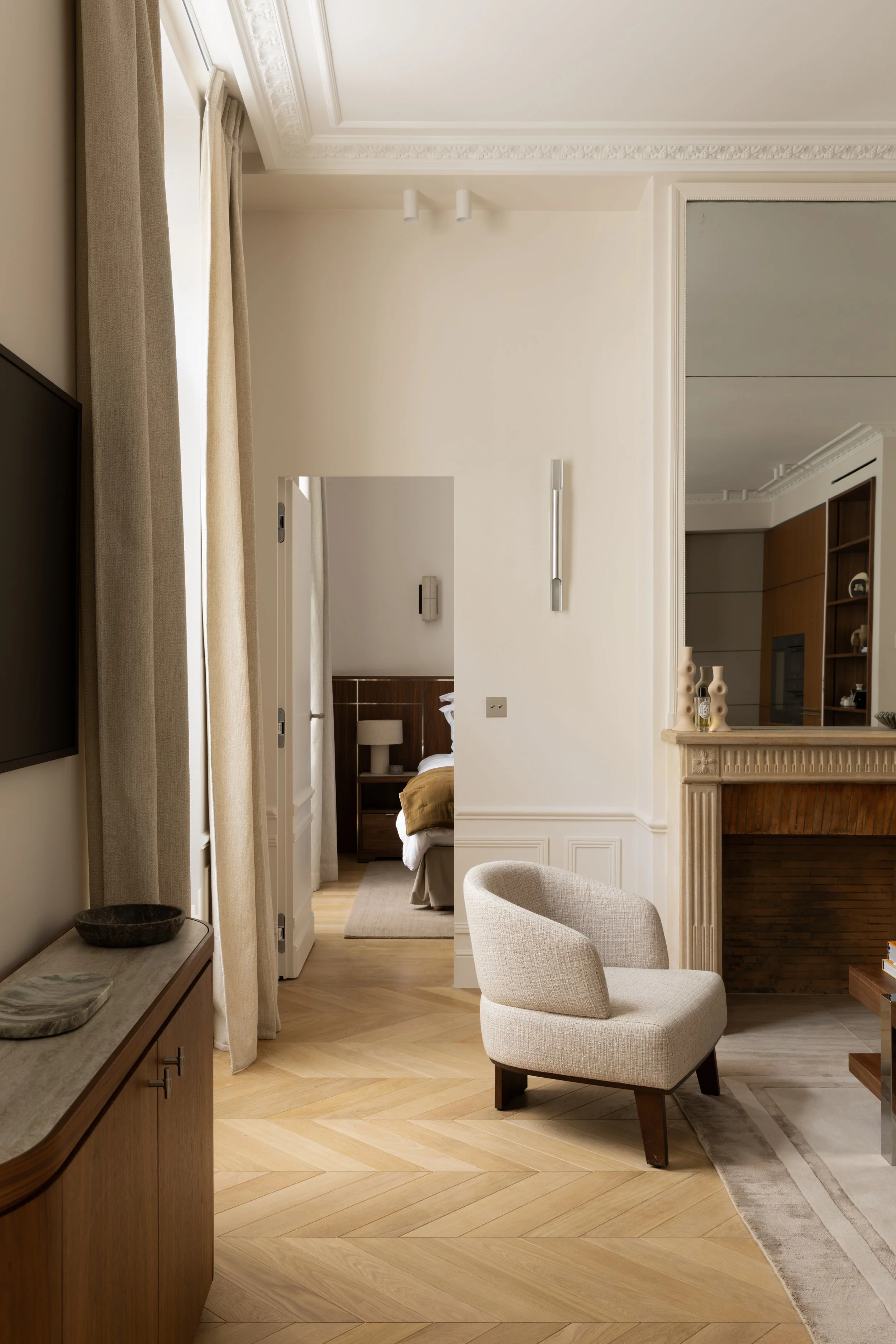 Salon parisien rénové avec fauteuil design, parquet en point de Hongrie, cheminée en pierre et décoration élégante – Intérieurs Chomet.
