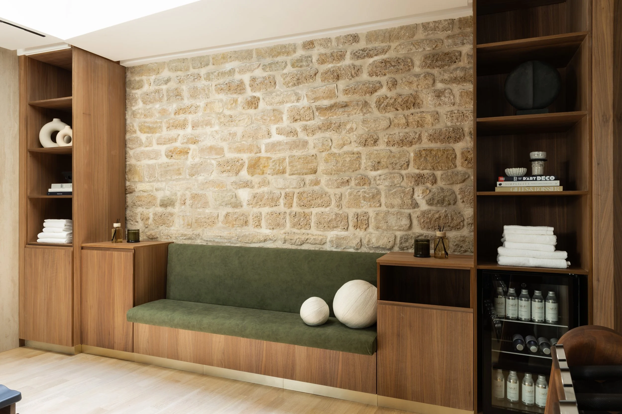 Banquette en velours vert, rangements en bois sur mesure et mur en pierre – Architecture d'intérieur haut de gamme à Paris.