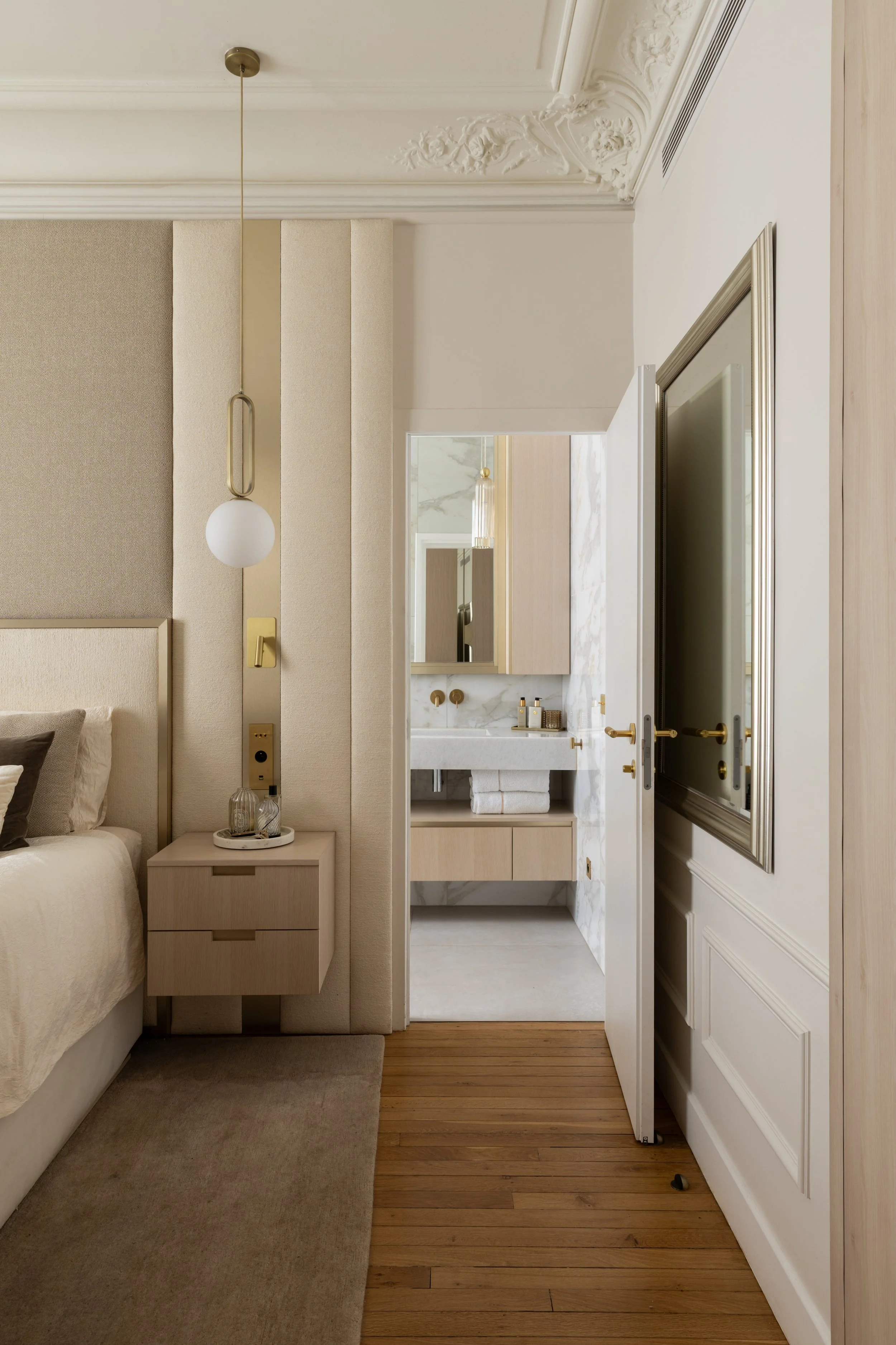 Vue depuis la chambre parentale vers la salle de bain attenante du projet Malesherbes à Paris, avec panneaux tapissés, chevet suspendu et surfaces en pierre blanche veinée — Intérieurs Chomet.