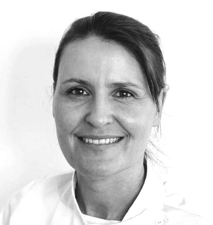 A black and white image of a dark haired woman, head and shoulders, dressed in a white therapist's jacket