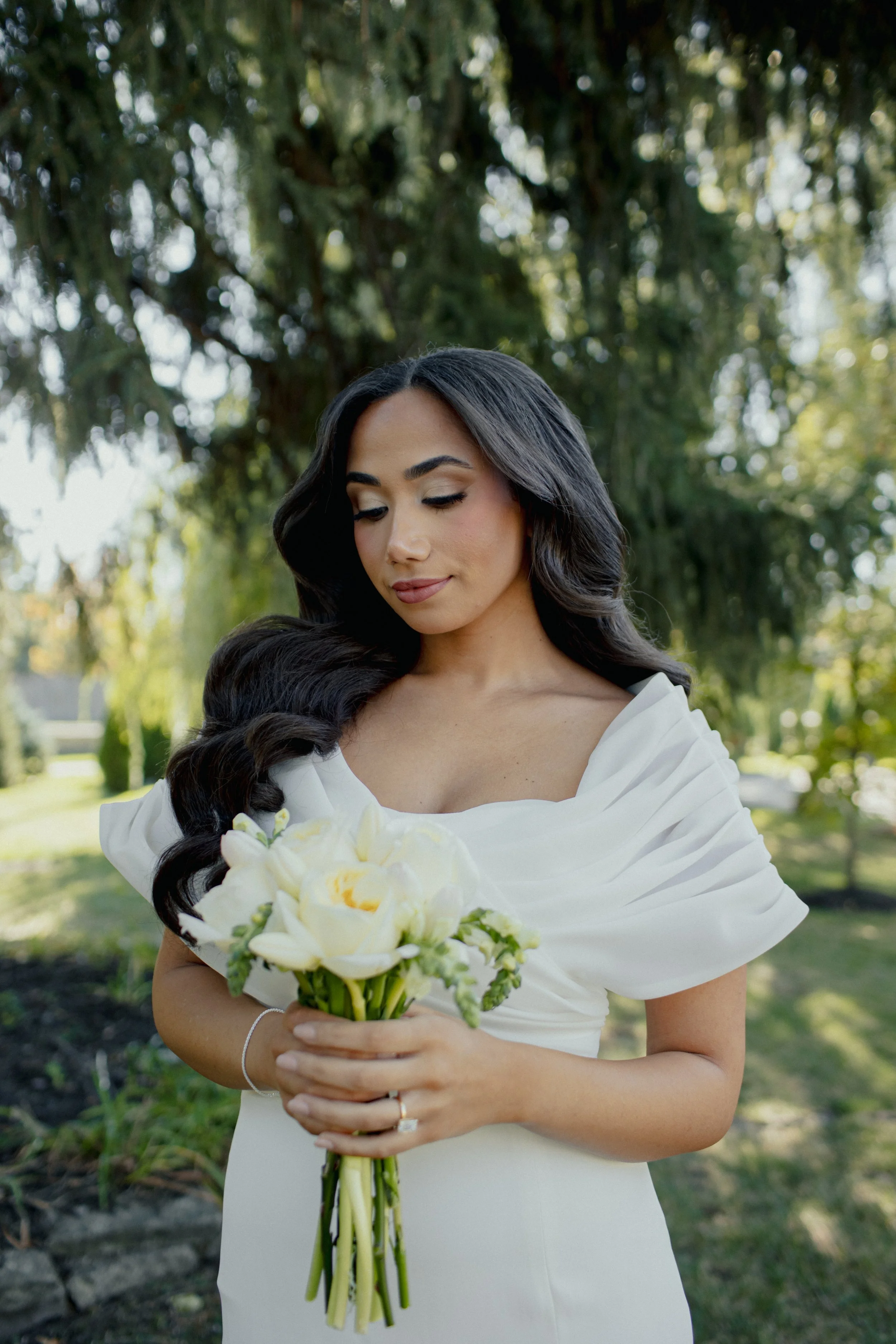A woman holding a bouquet of white flowers in a park setting with trees.