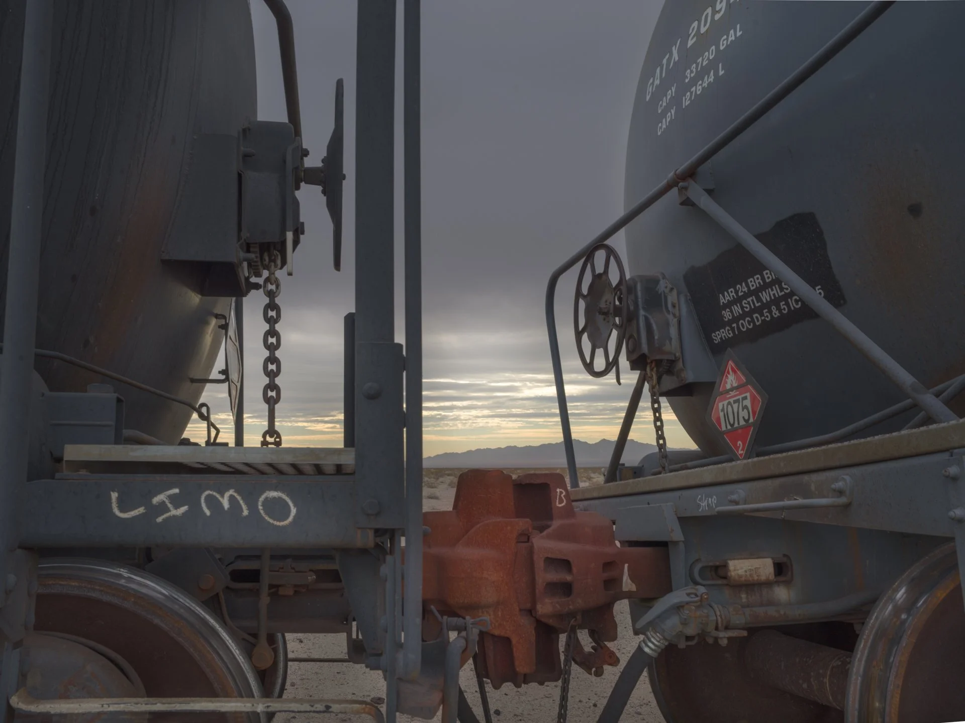 Close-up view of two large metallic tanks on a trailer in a desert landscape during sunset, with cloudy sky and distant mountains.