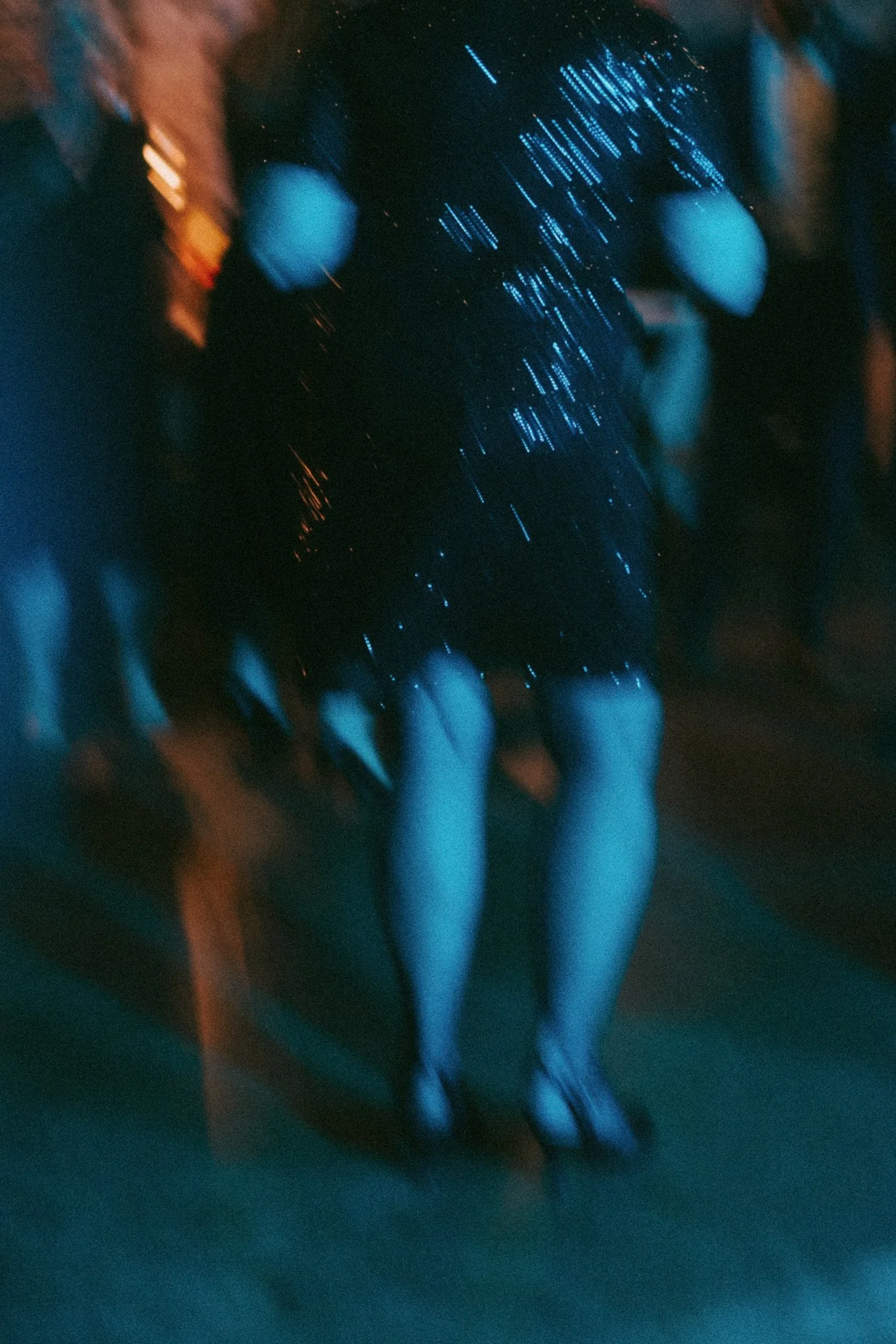 Close-up of a person's hand with blue and orange neon lights reflecting on the fingers at night.