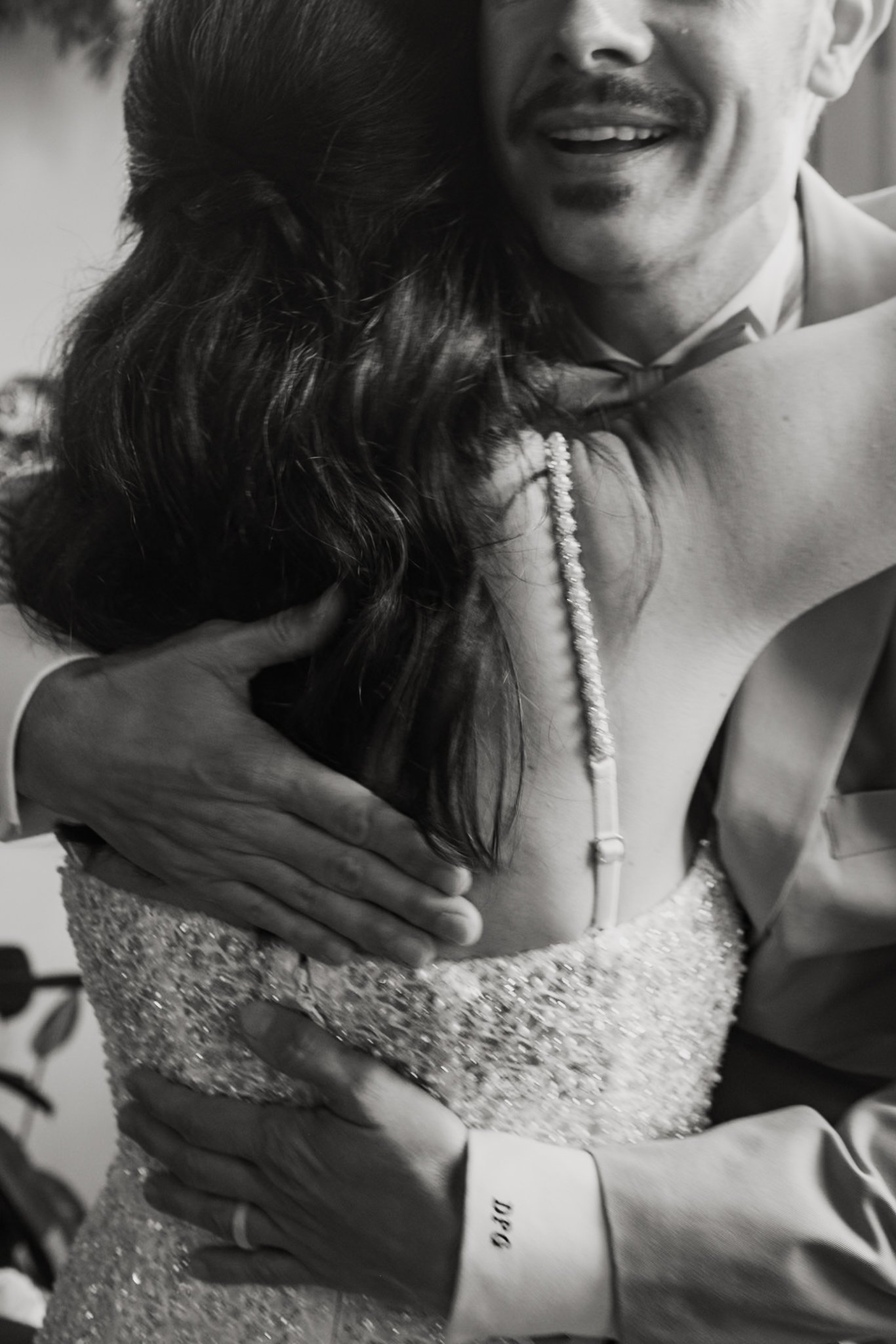 A couple embracing, with the woman wearing a sparkly dress and the man in tuxedo with a bow tie, smiling at each other
