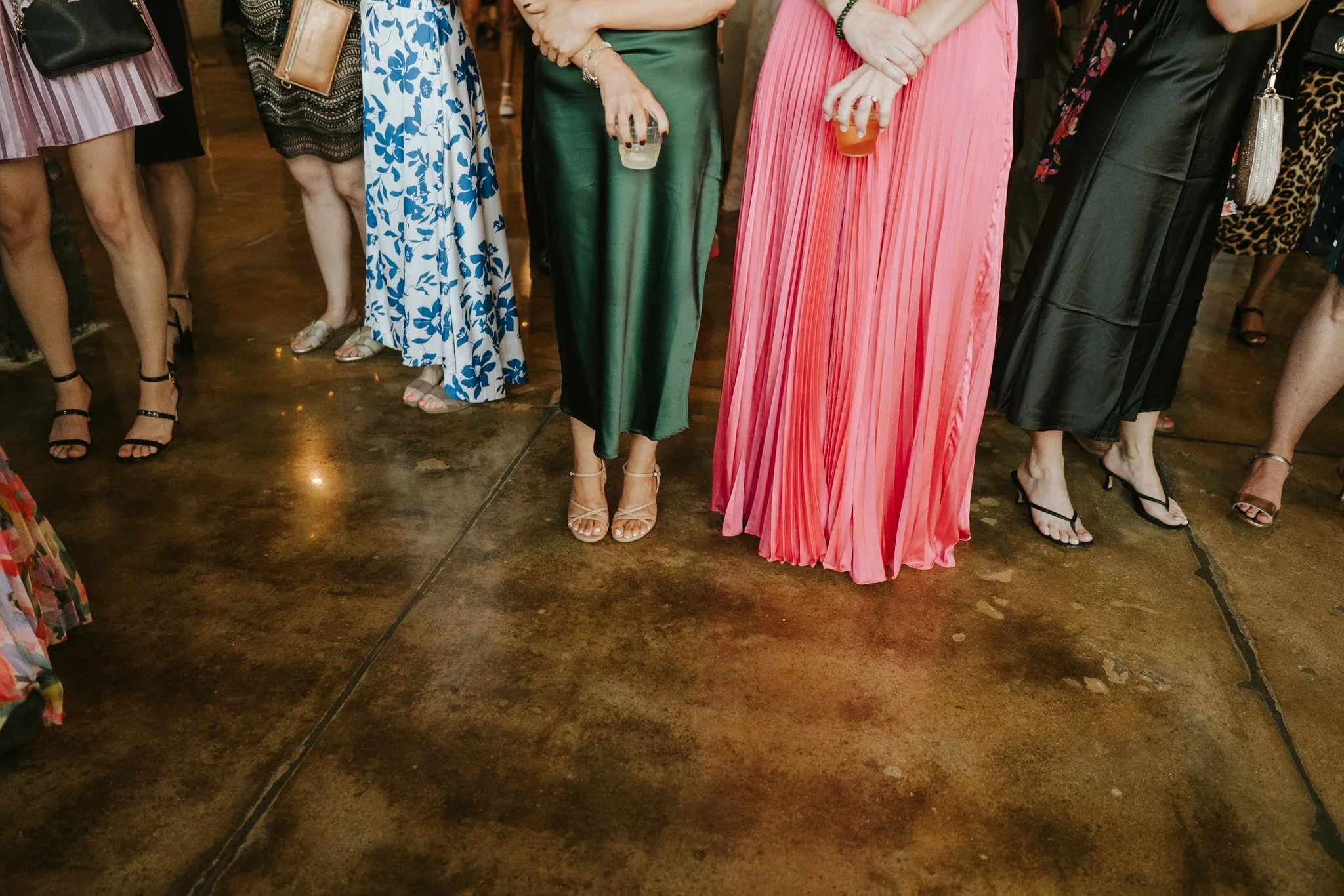 Group of women standing in a line at a social gathering, wearing colorful dresses and holding drinks.