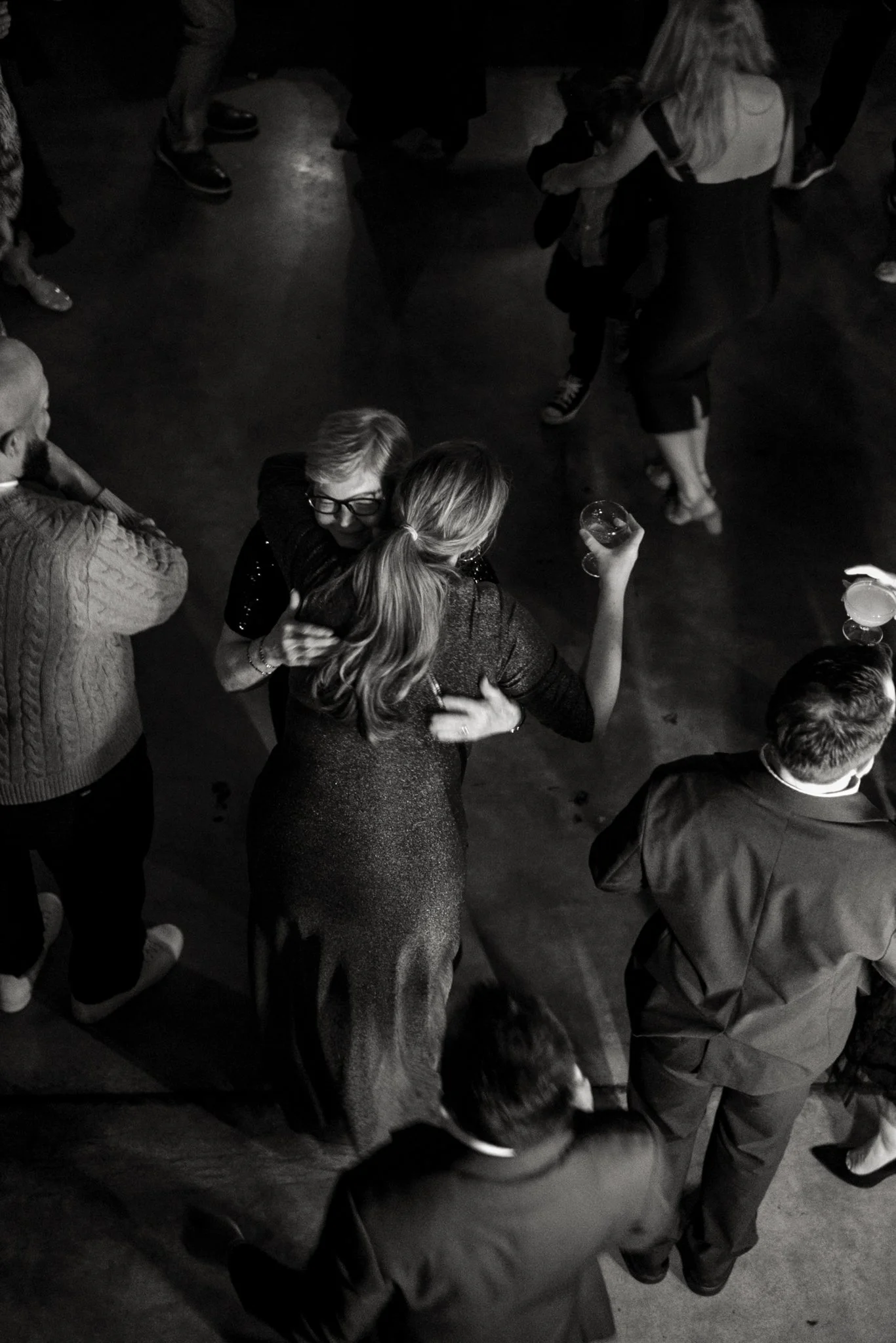 Group of people socializing at a party, some holding drinks, in a dimly lit setting.