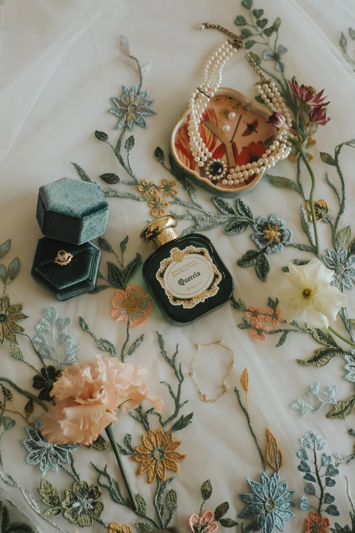 Close-up of embroidered floral tablecloth with jewelry and perfume bottles on top.