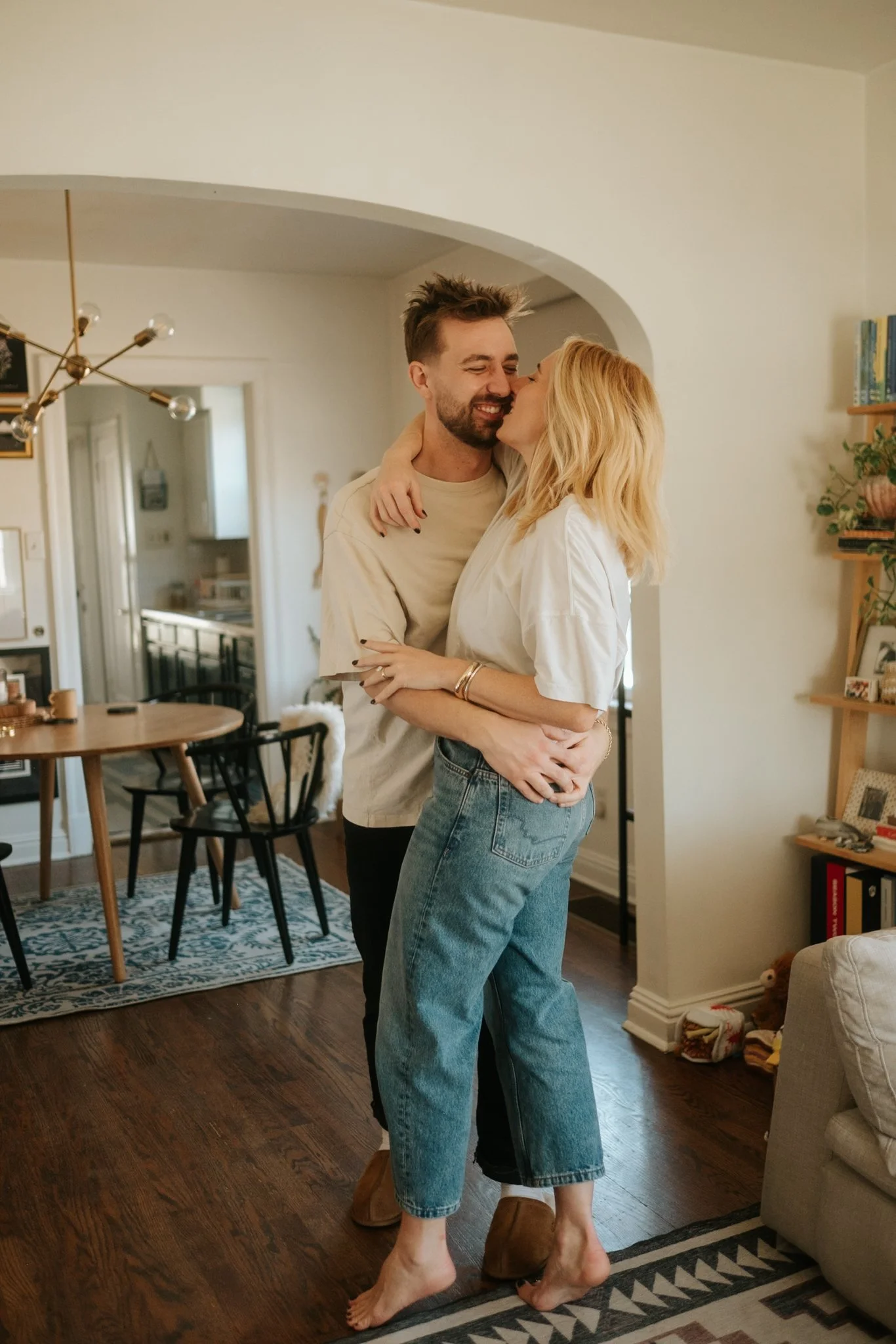 A couple hugging and embracing in a cozy, well-lit living room, smiling at each other.