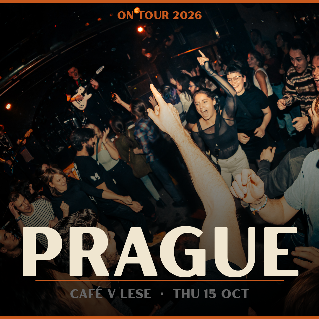 People dancing and enjoying a live band performance at a nightclub, with orange and black lighting, promoting a Prague concert on October 15, 2026.