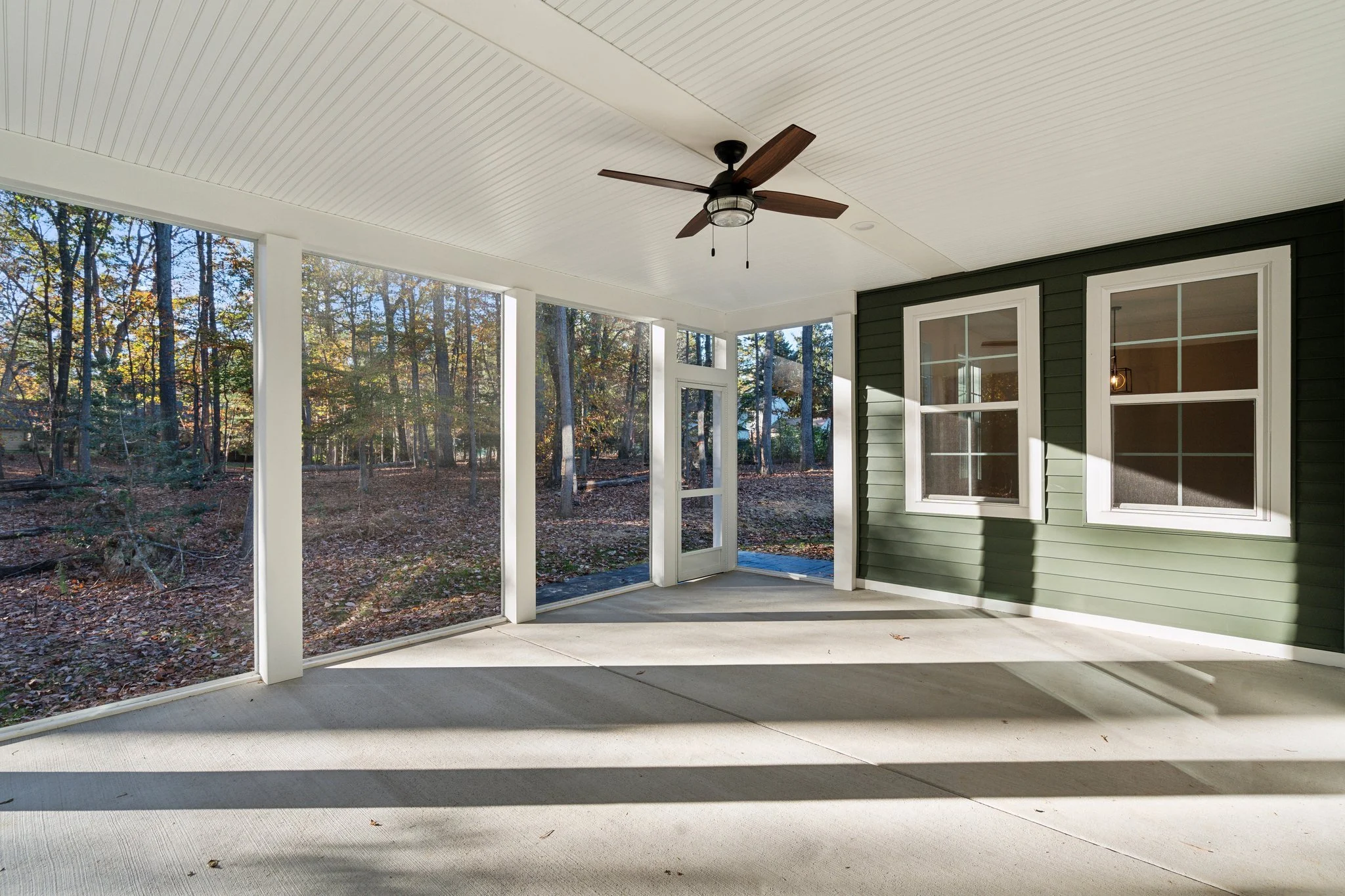 Covered porch with a ceiling fan overlooking a wooded backyard.