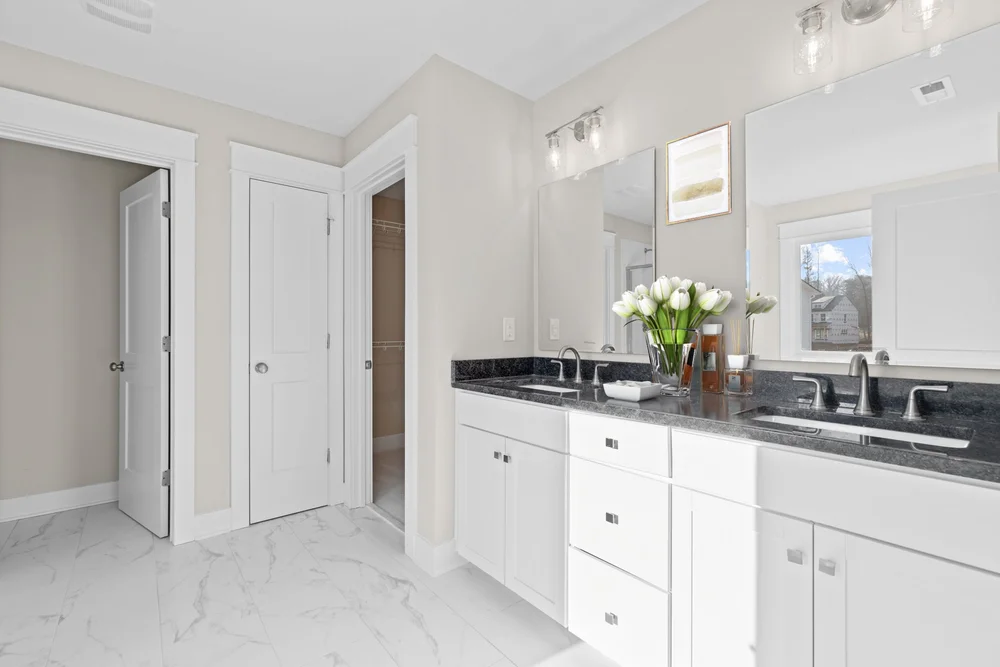Modern bathroom featuring double sinks, white cabinetry, and sleek black countertops with a spacious layout.
