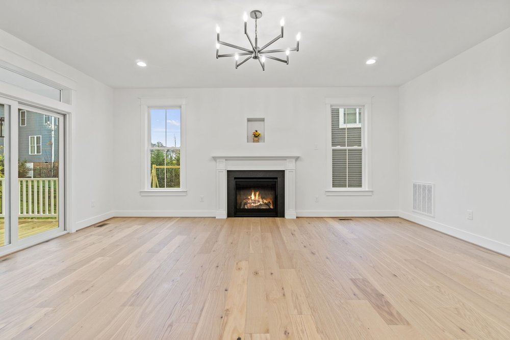 Spacious family room featuring hardwood floors, a modern chandelier, and a fireplace centered between two windows.