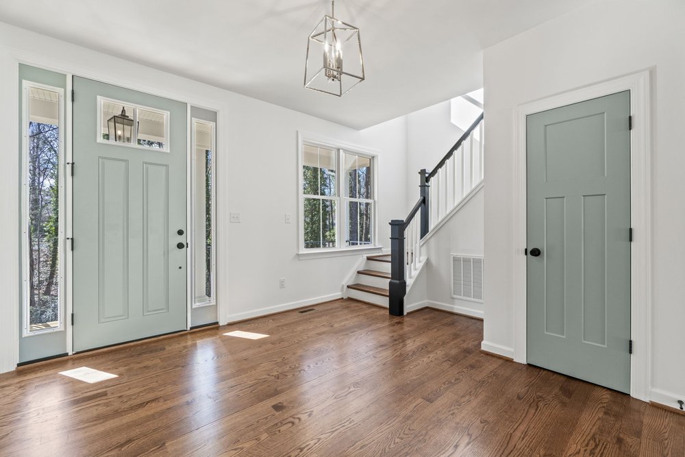 Entryway with hardwood floors, green double doors, staircase, and chandelier lighting.