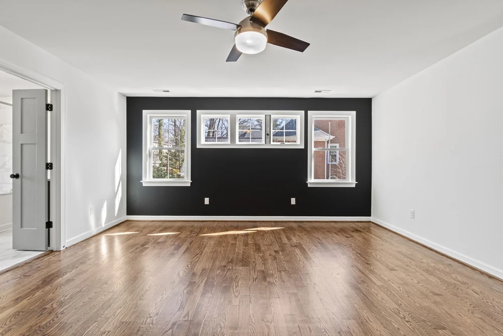 Bedroom with hardwood floors, ceiling fan, large windows, and a dark accent wall.