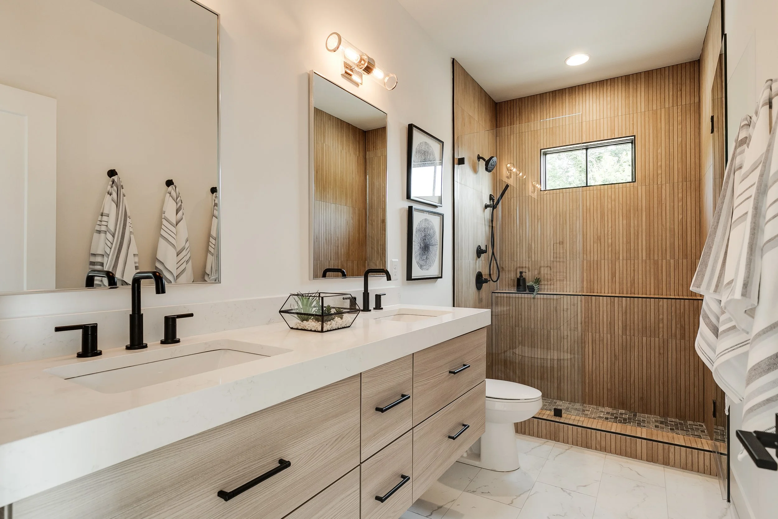 A modern bathroom with a large double vanity, black fixtures, and a walk-in shower with a wood-like tile wall. (Copy)