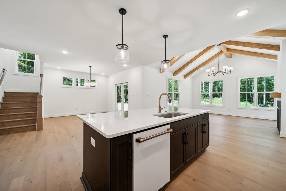 View of Dark Kitchen Island, Dining Room, and Living Room with Wood Beams in the Vero