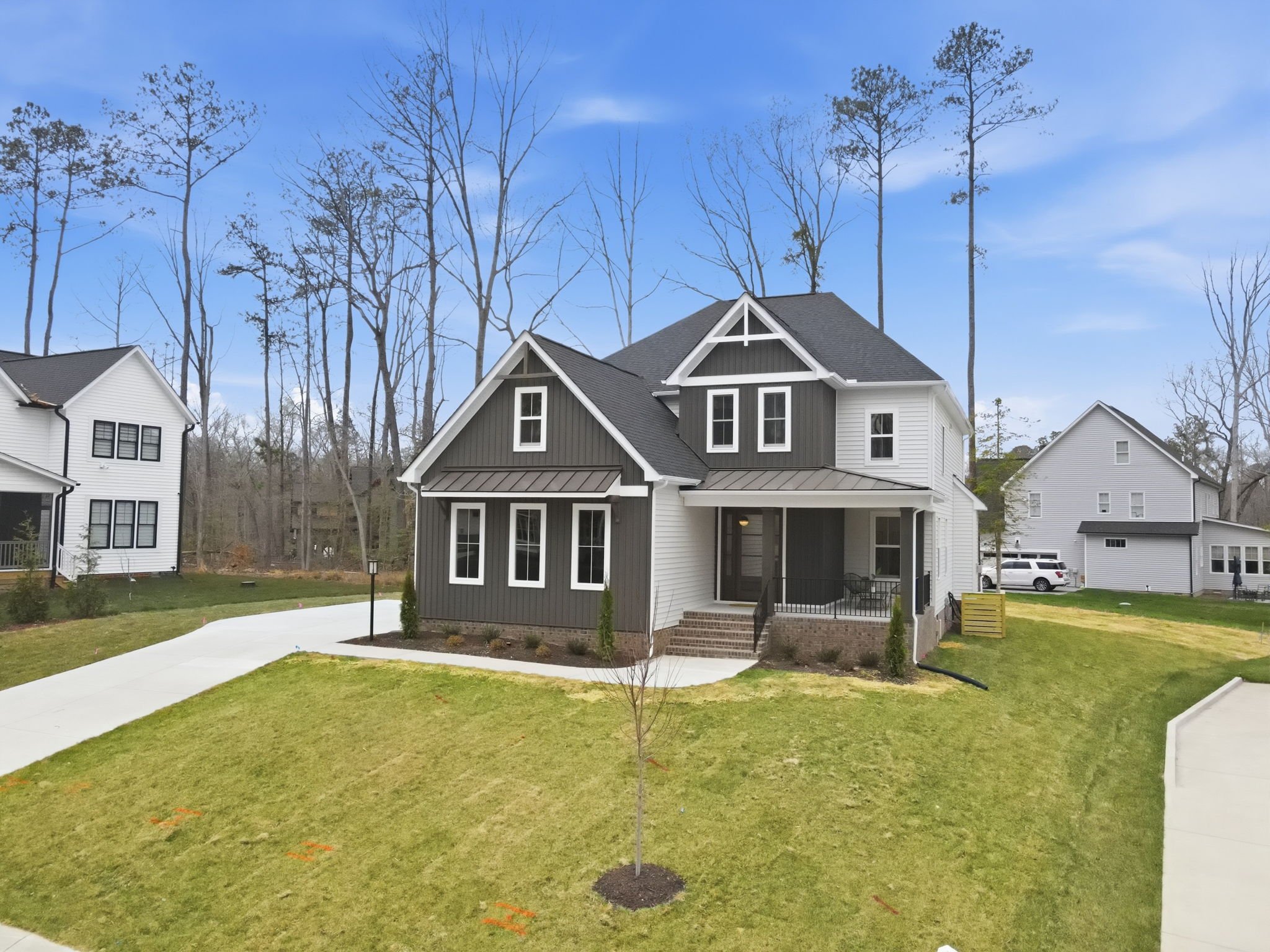 Newly landscaped front yard with young tree, grass, and sidewalk in front of modern house, under a partly cloudy blue sky.