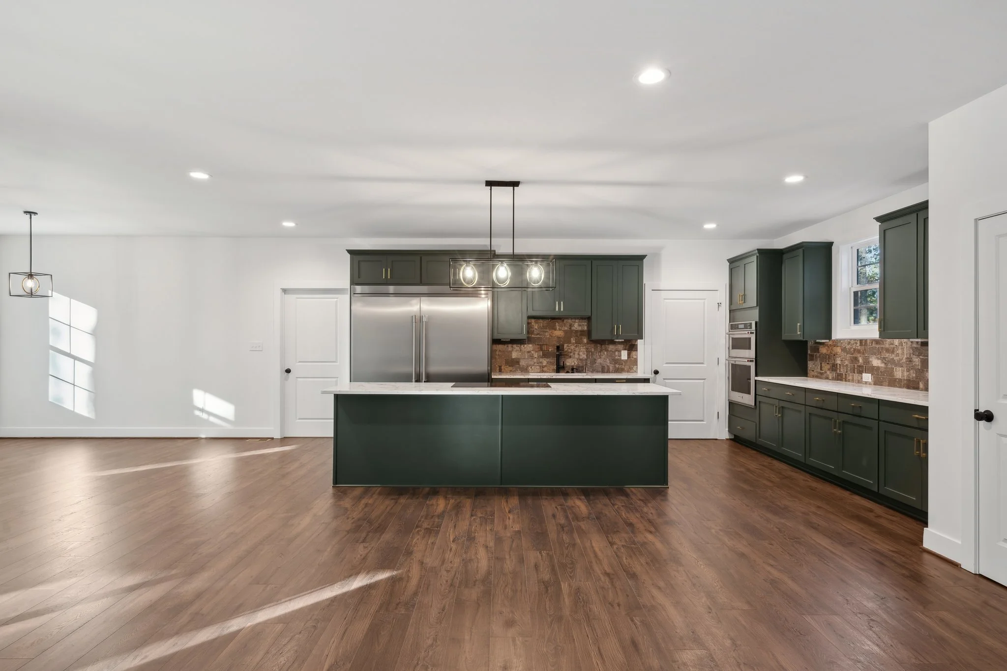 Spacious kitchen with a dark green island and hardwood floors.