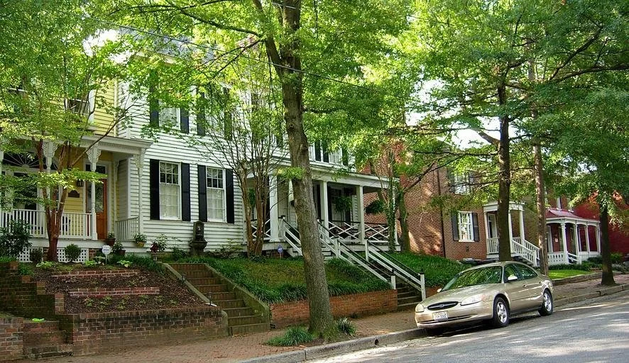 Street view with trees, residential houses, and a parked silver car.